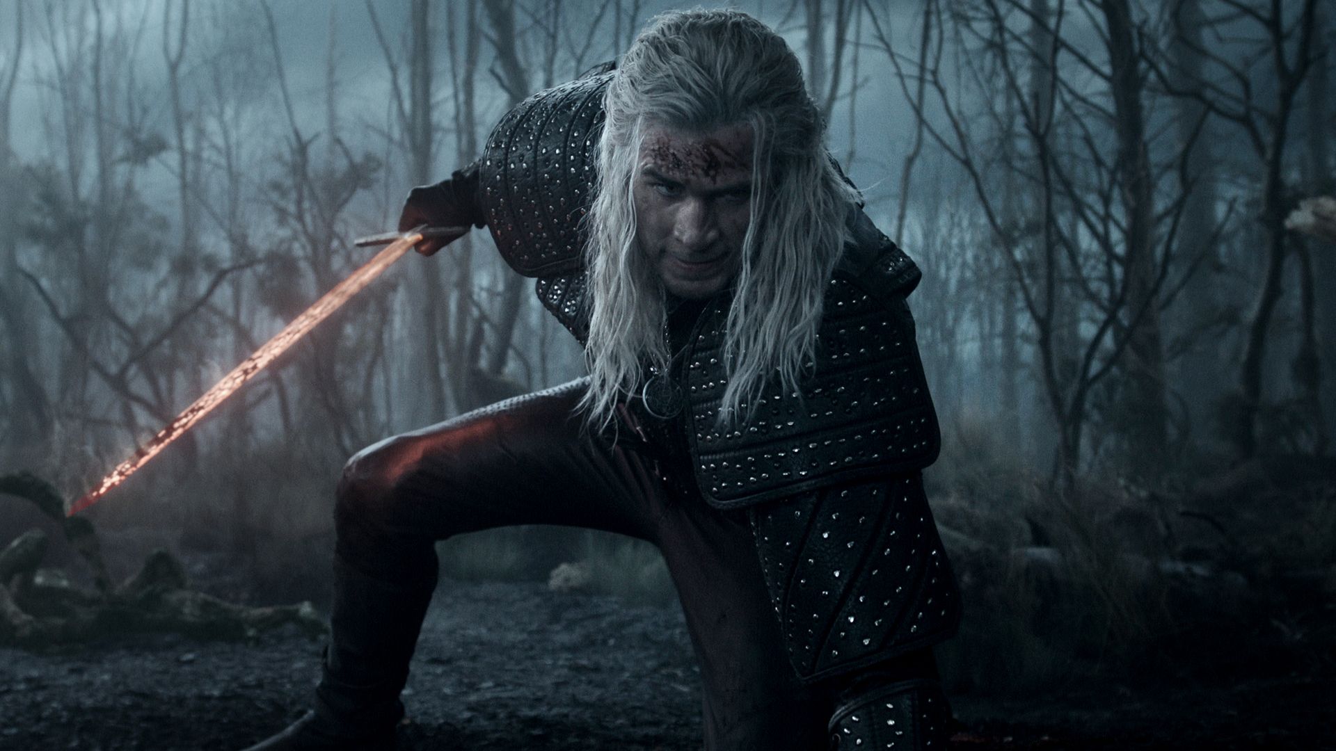A warrior with long white hair and black studded armor crouches with a glowing fiery sword in a dark, foggy forest with bare trees. He has blood on his face and an intense gaze.
