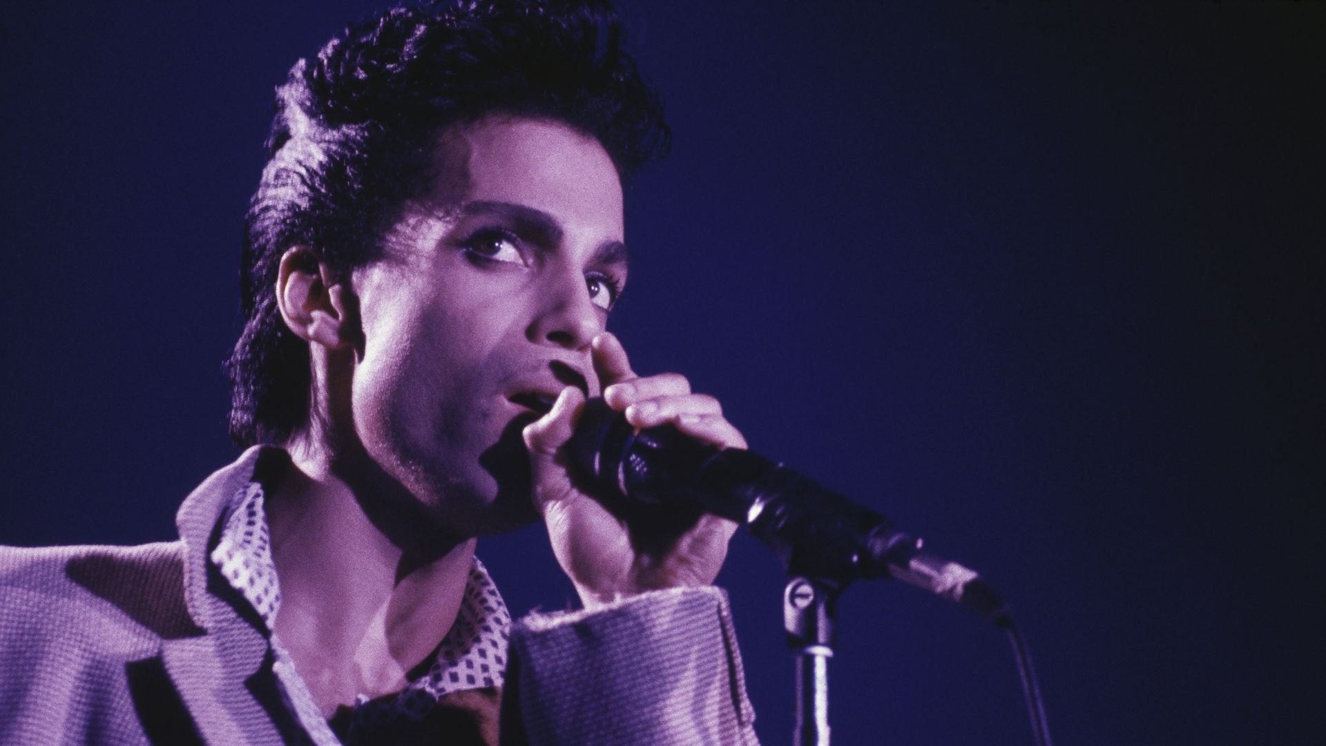PRince in purple lighting singing into a mic