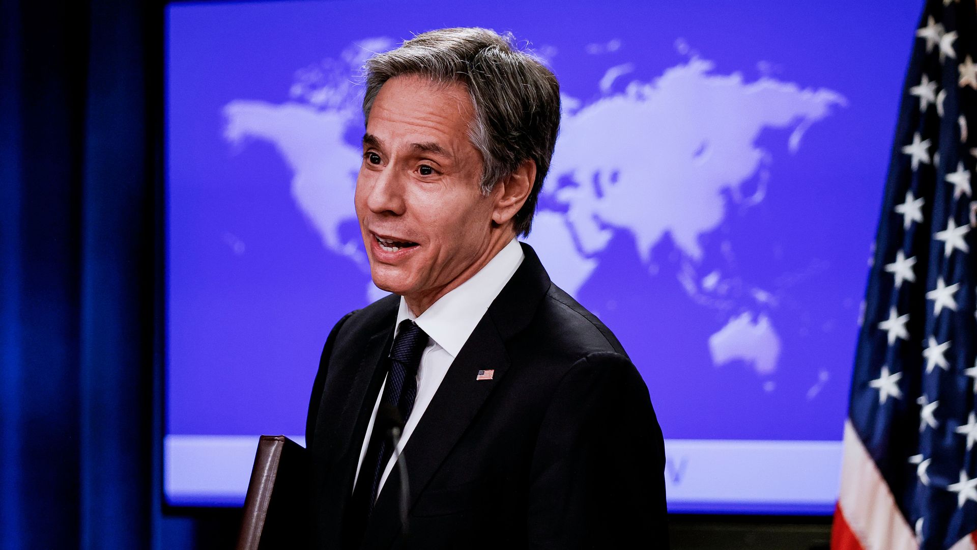 U.S. Secretary of State Antony Blinken stands in front of a world map.