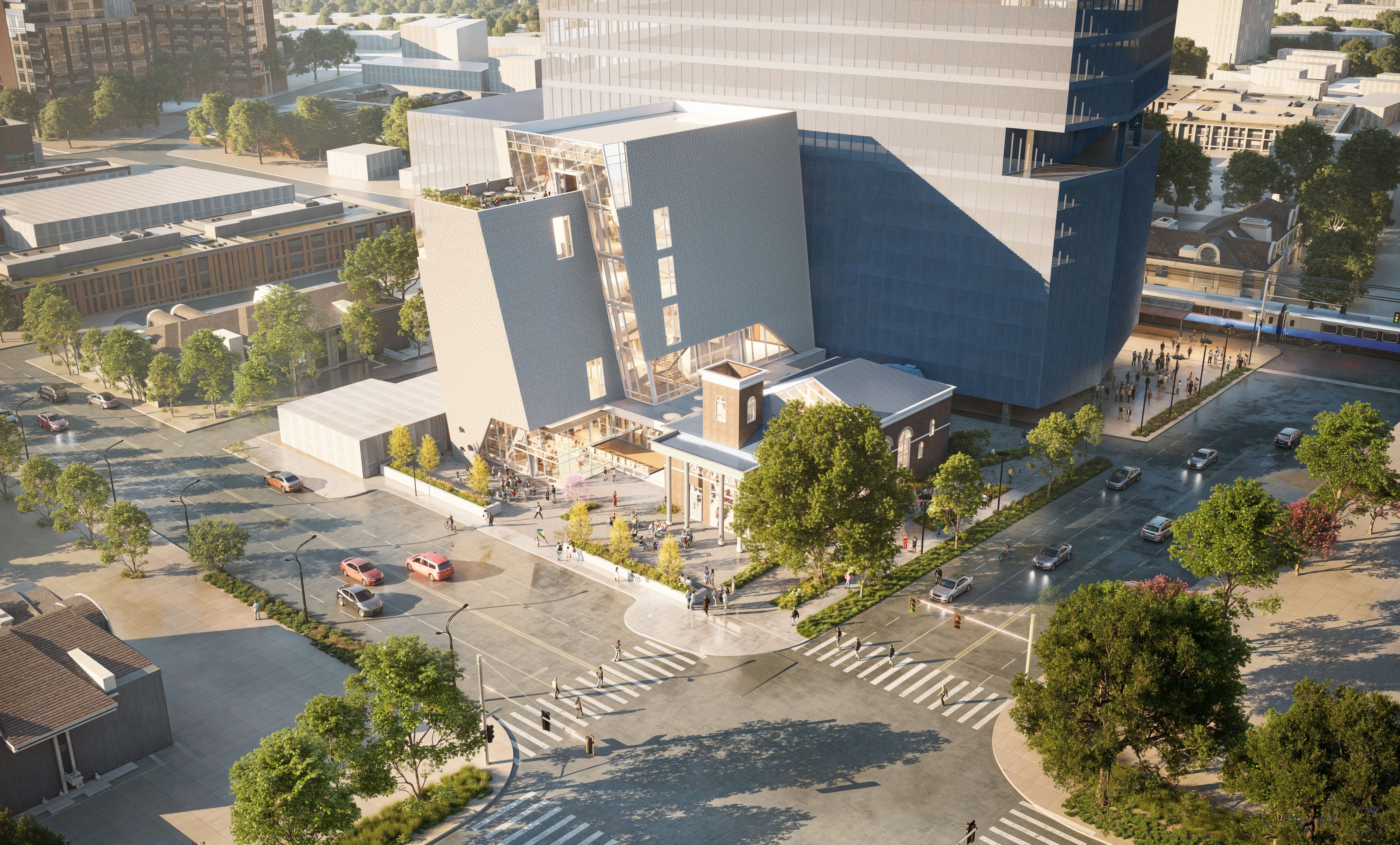 A modern cityscape showing a large, angular gray and glass building next to a smaller historic brick building with a tower. People walk on sidewalks and crosswalks along tree-lined streets with cars.
