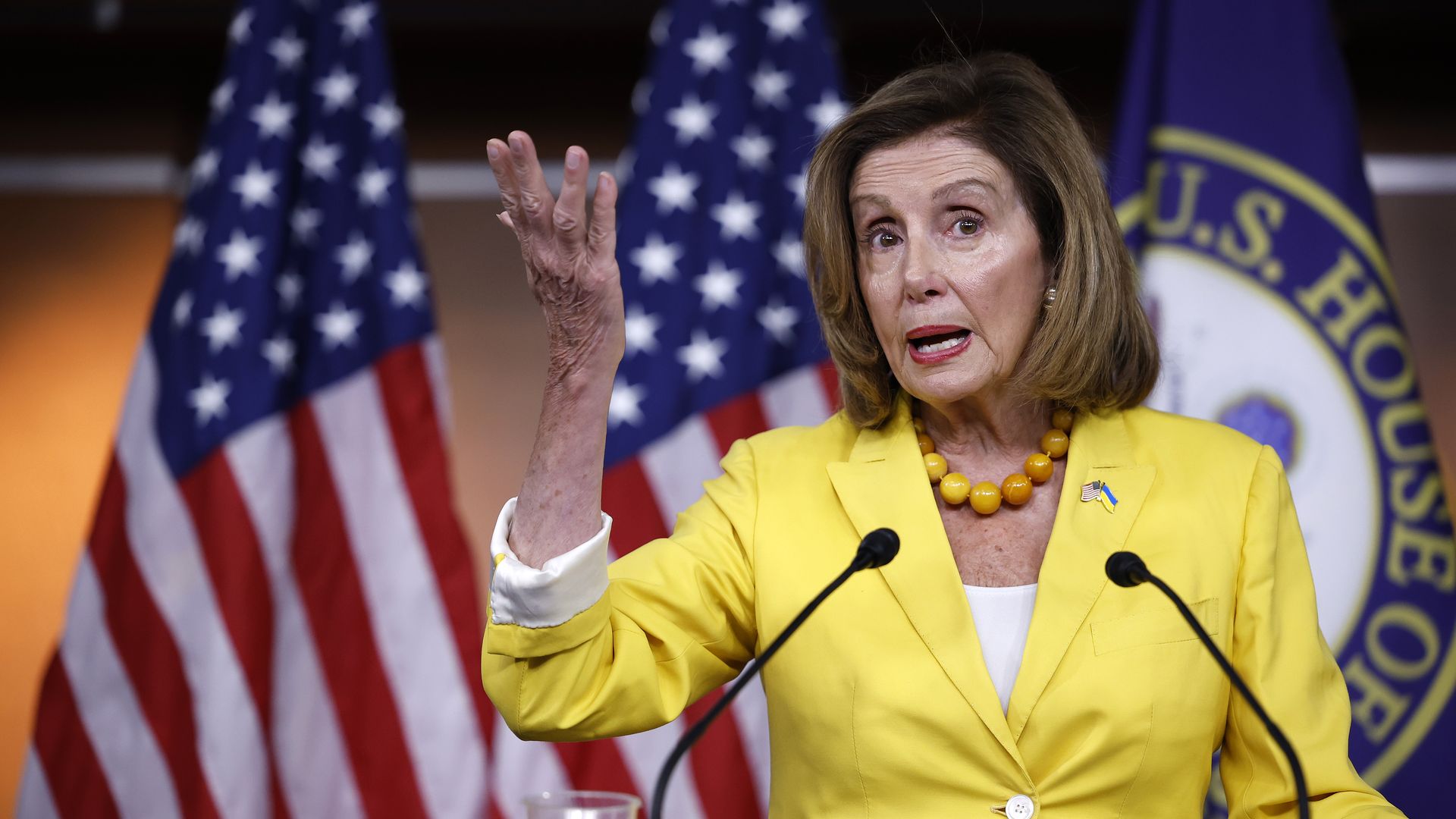 Nancy Pelosi in a yellow suit speaks in the House of Representatives