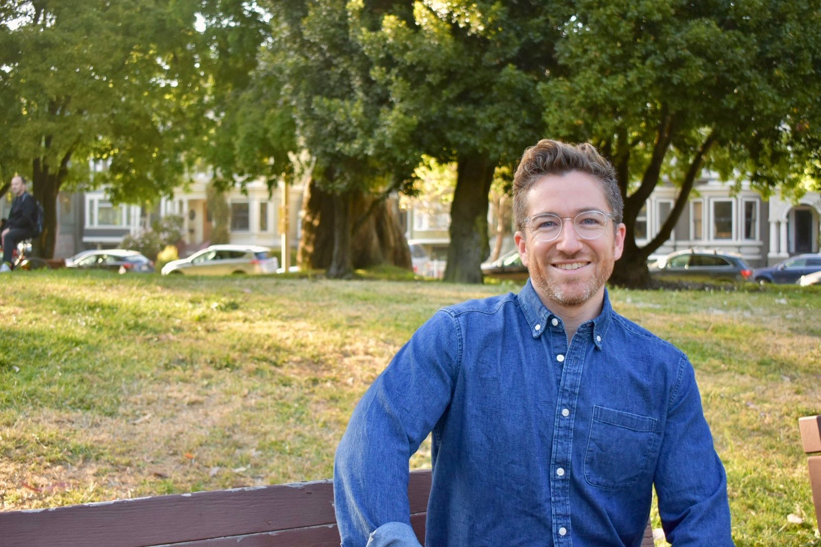 man smiling in park, sitting on grass