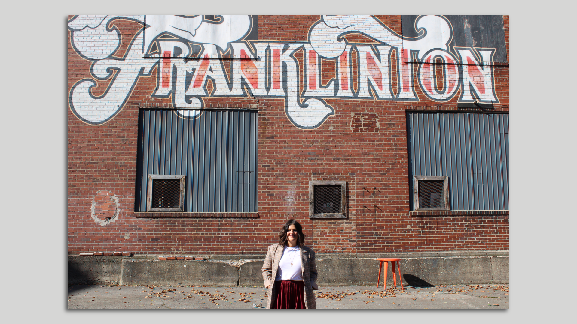 Rebecca Asmo stands in front of a mural that says "Franklinton" on a brick wall