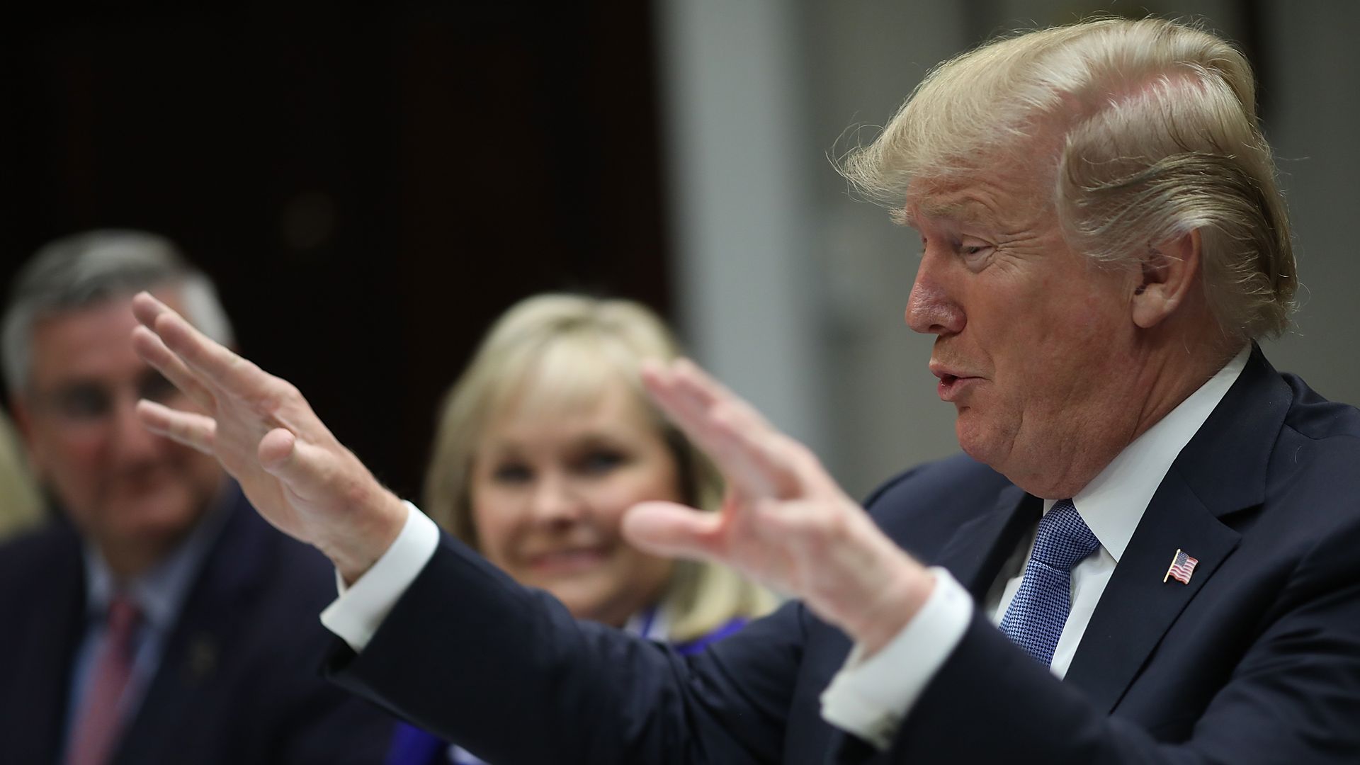 President Donald Trump sits at a table and gestures with both his hands forward.