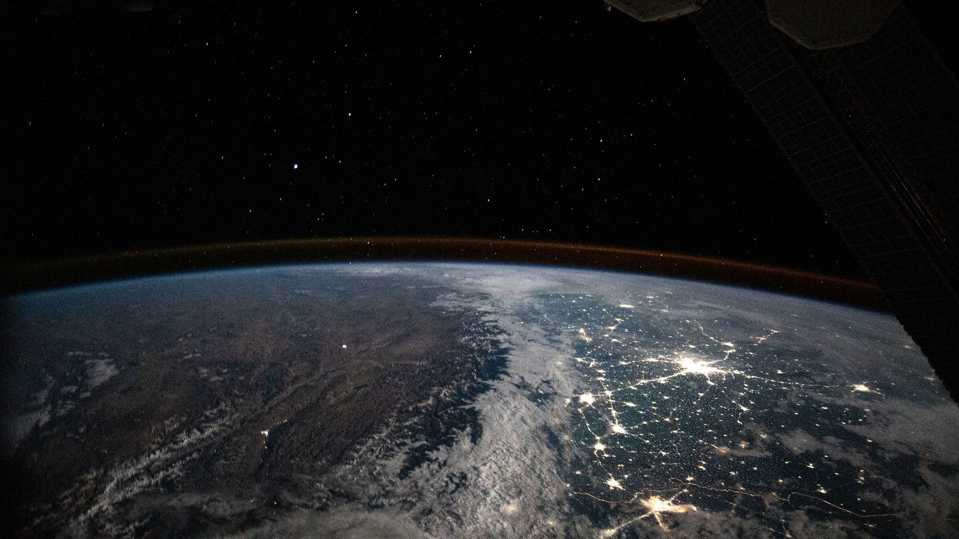 The earth seen from the International Space Station, with city lights distantly connected on the surface of the planet 