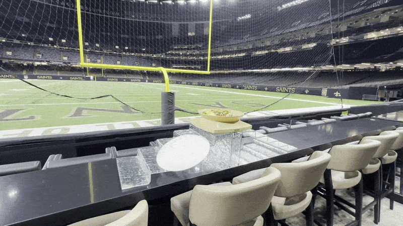 A video moves closer to a Superdome-shaped bowl of nachos. The bowl is placed on a bar top within seating near the end zone.