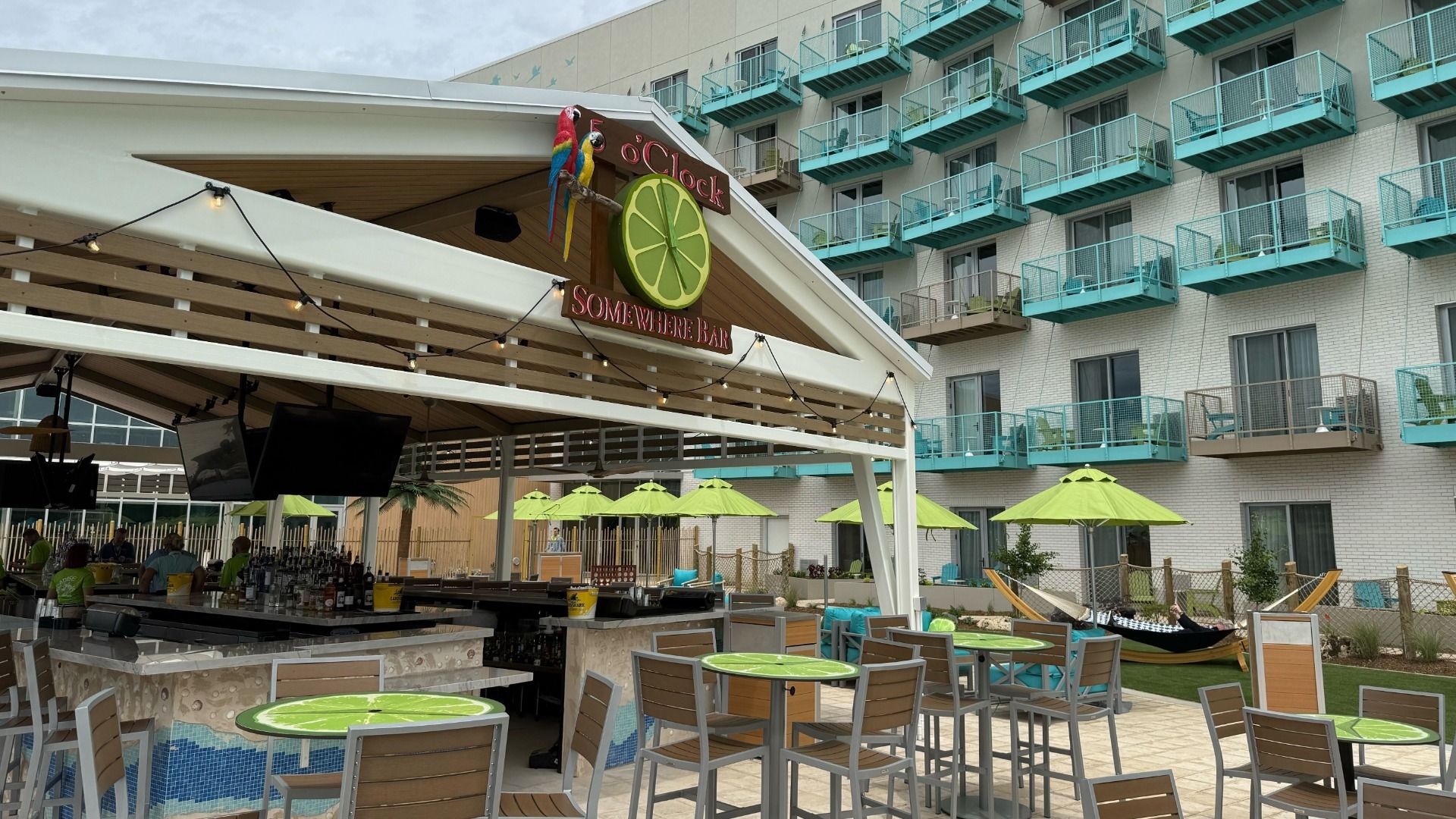 Photo shows the Margaritaville pool deck with bright green and teal accent colors and the 5 o'clock somewhere bar and grill in the foreground.