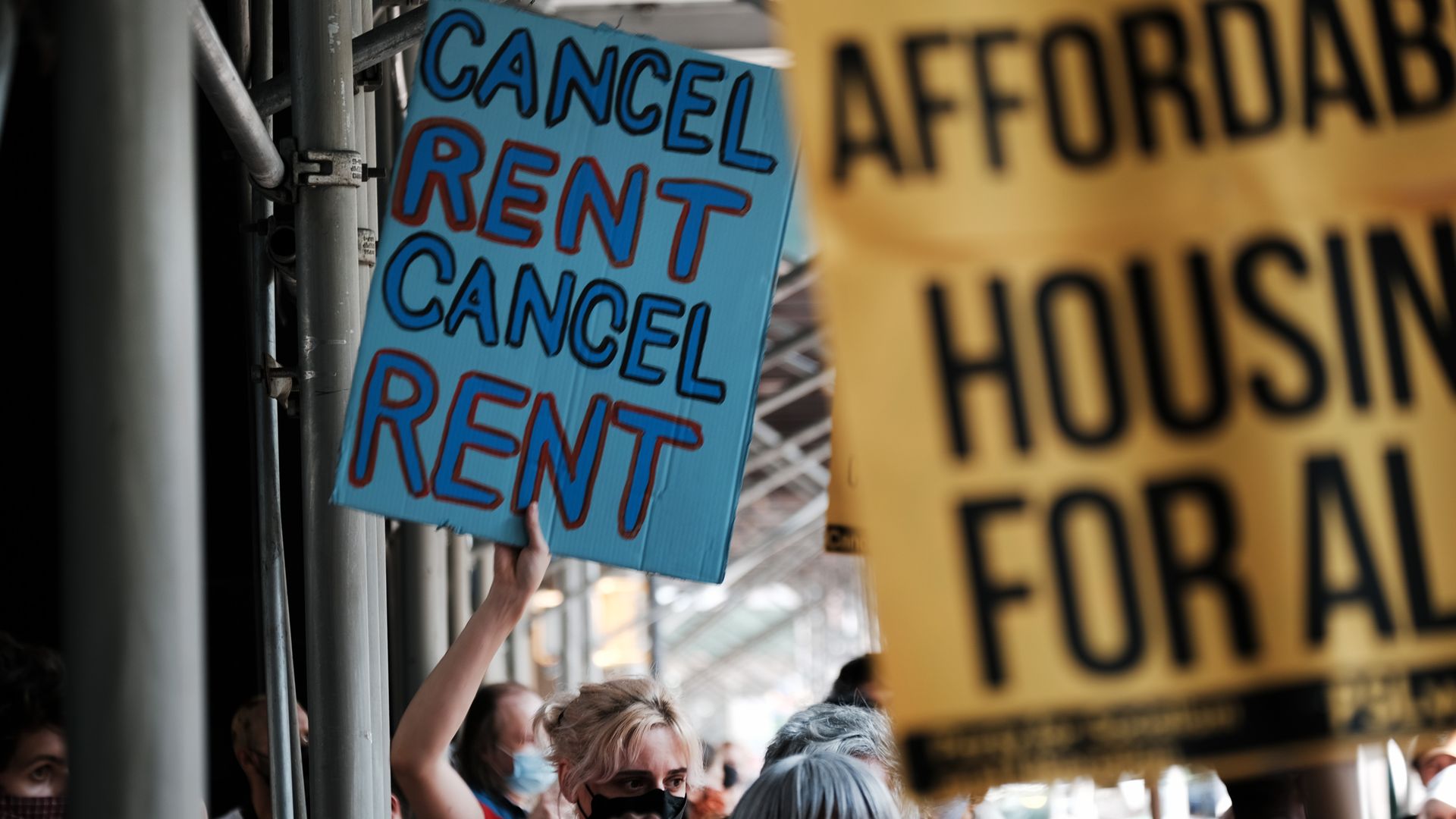 Photo of a protester holding a sign that says "Cancel rent" at an outdoors demonstration