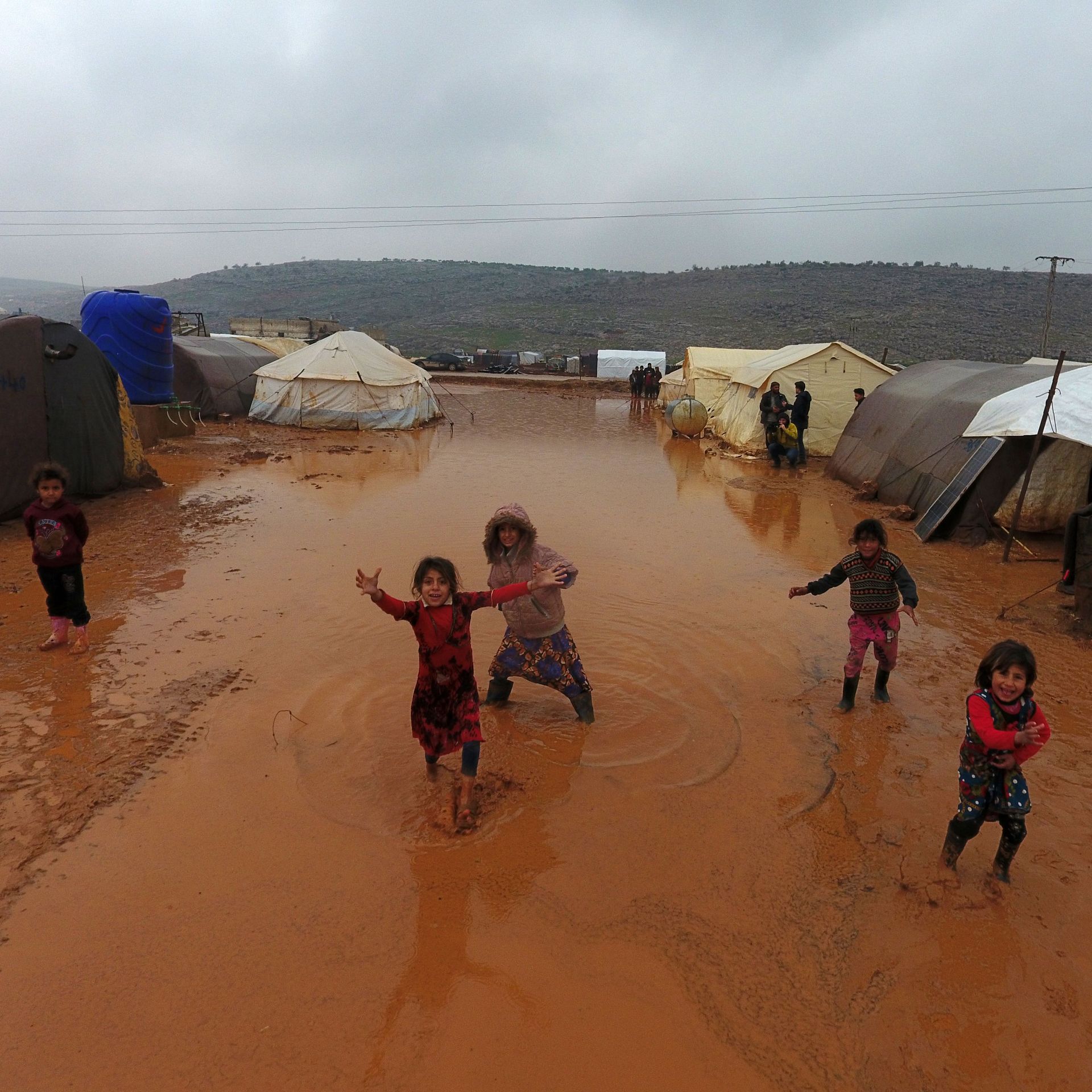 children playing in between tents on wet ground of refugee camp