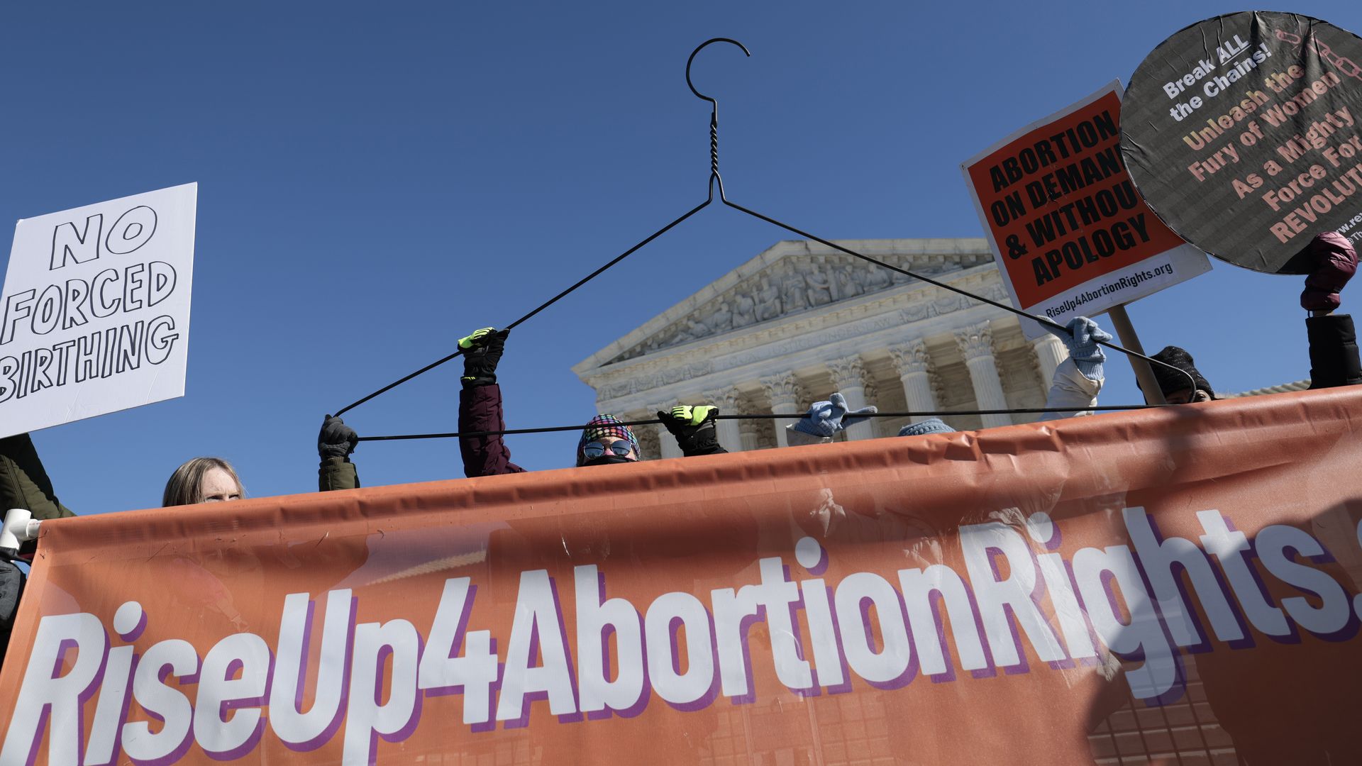 Photo of protesters holding an orange banner that says "RiseUp4AbortionRights"