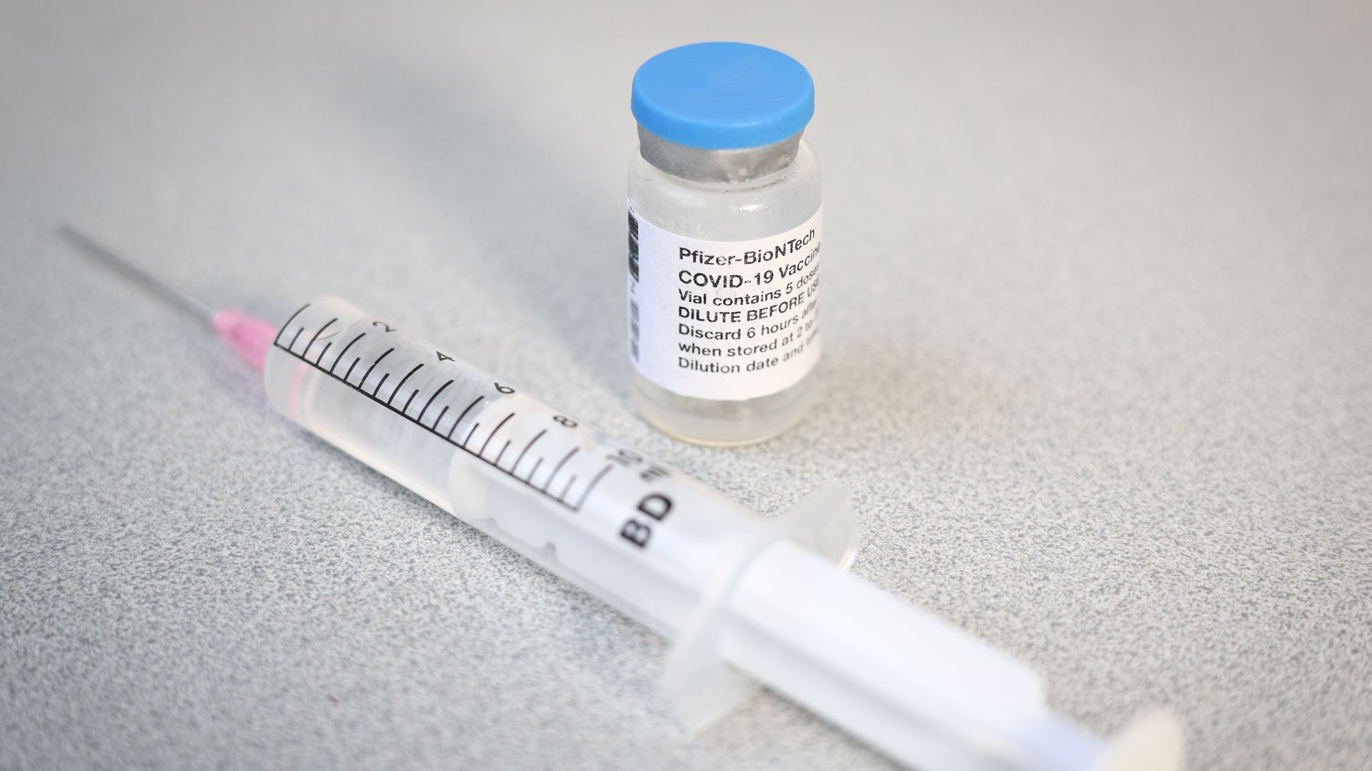 A vial with a Pfizer label is seen with a syringa and needle
