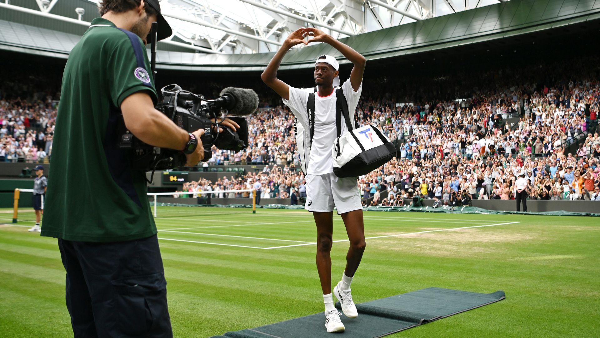 Tennis player Christopher Eubanks holds his hands in a heart shape as he walks off a grass tennis court at Wimbledon