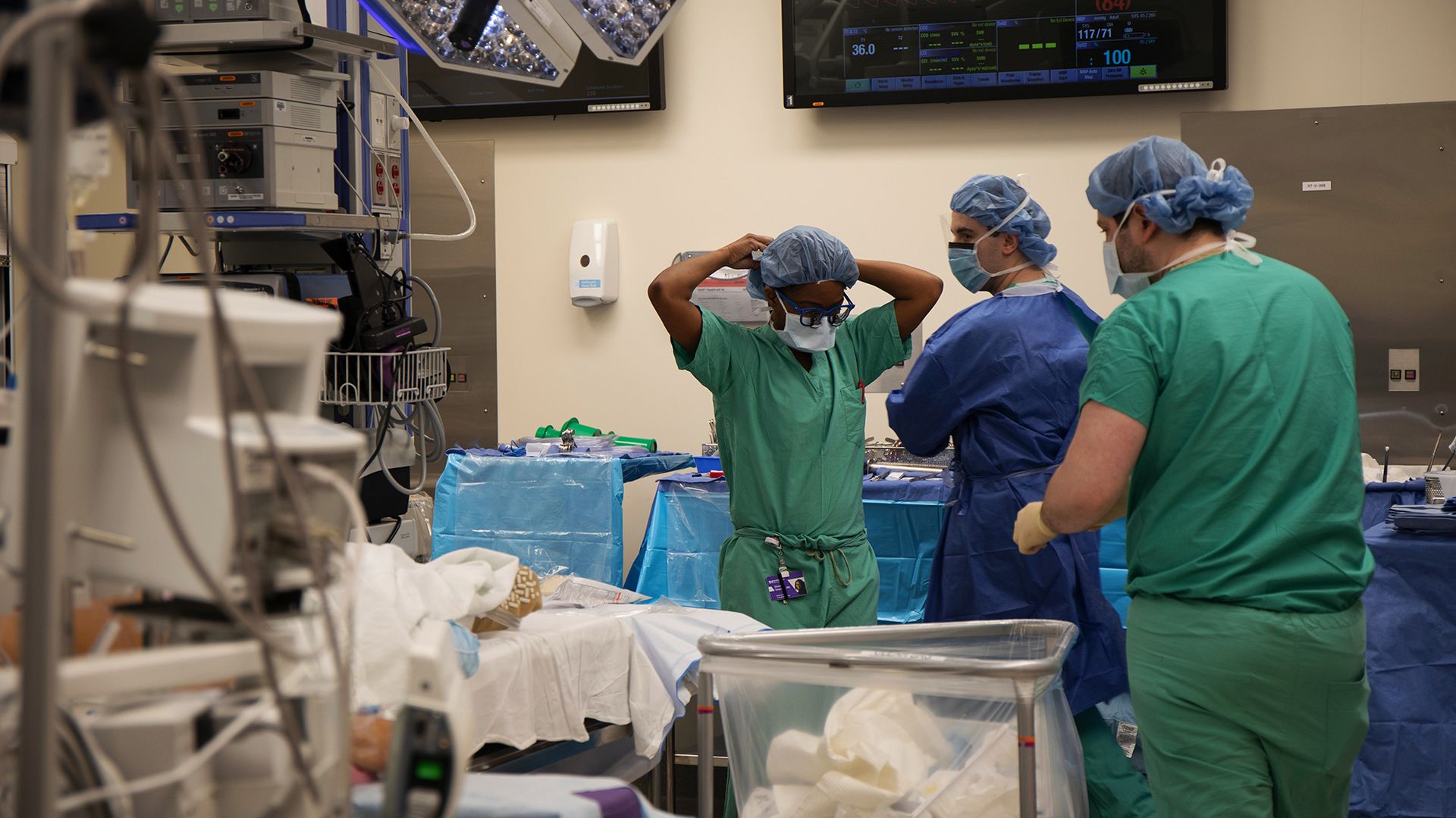 Photo of three doctors in scrubs standing around a patient's bed preparing for surgery