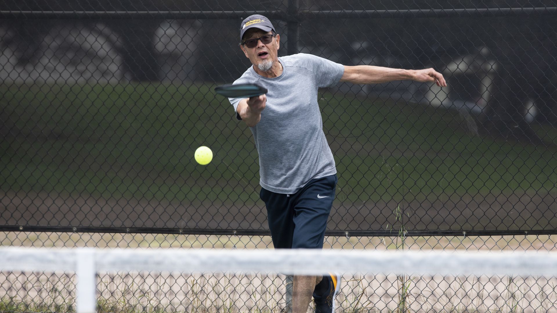 Photo of a person hitting a pickleball with a racket on a tennis court 