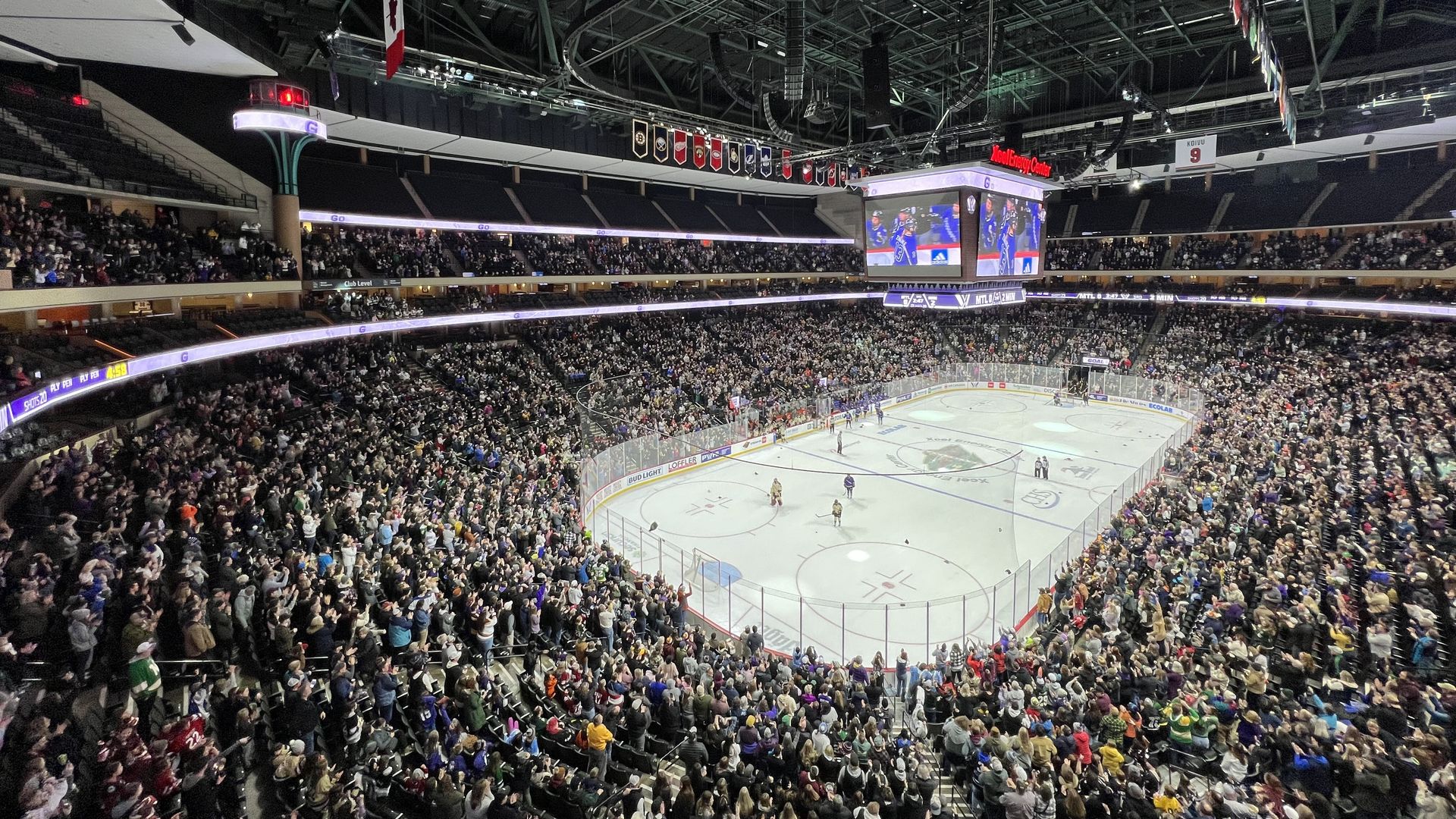 A hockey arena with a white ice sheet and a crowd, filling the lower two-thirds of the stadium, standing and applauding.