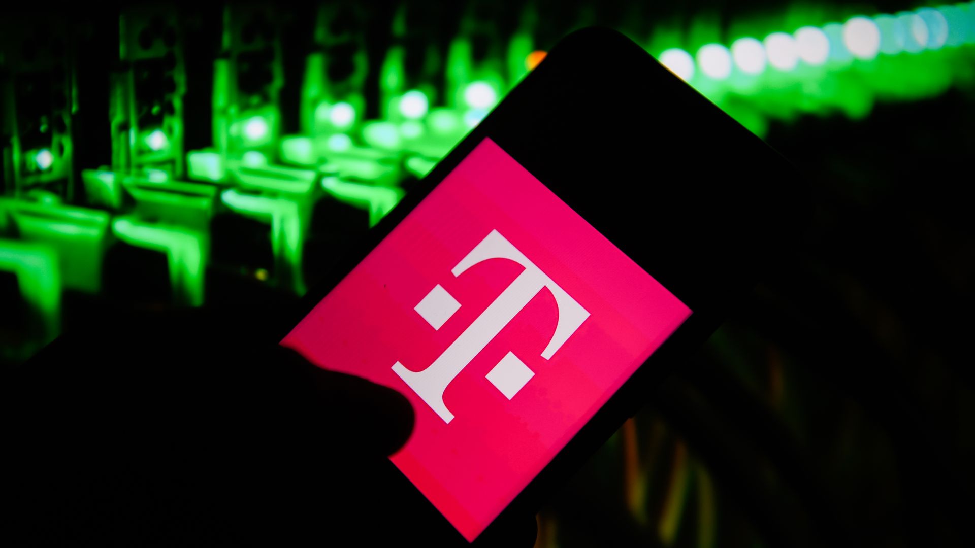 The t mobile on a logo on a phone in the foreground. A dark background.