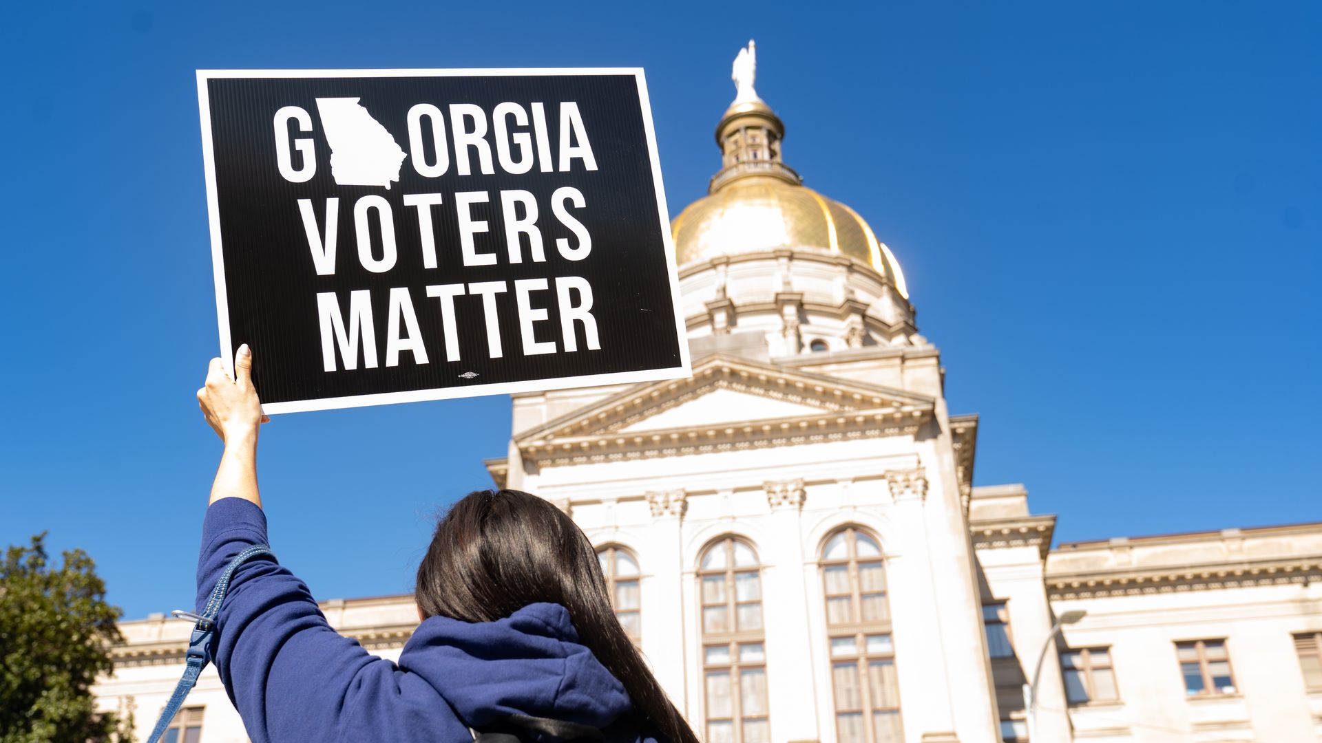 Photo of a person holding up a sign that says "Georgia voters matter" with the Georgia state capitol building in the backdrop