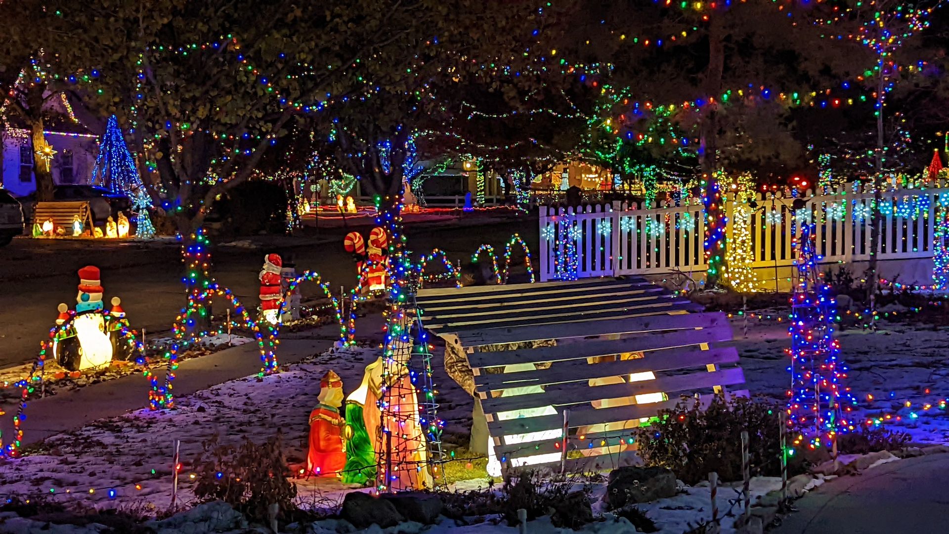 A light-up manger scene stands in a front yard in a neighborhood covered with Christmas lights.