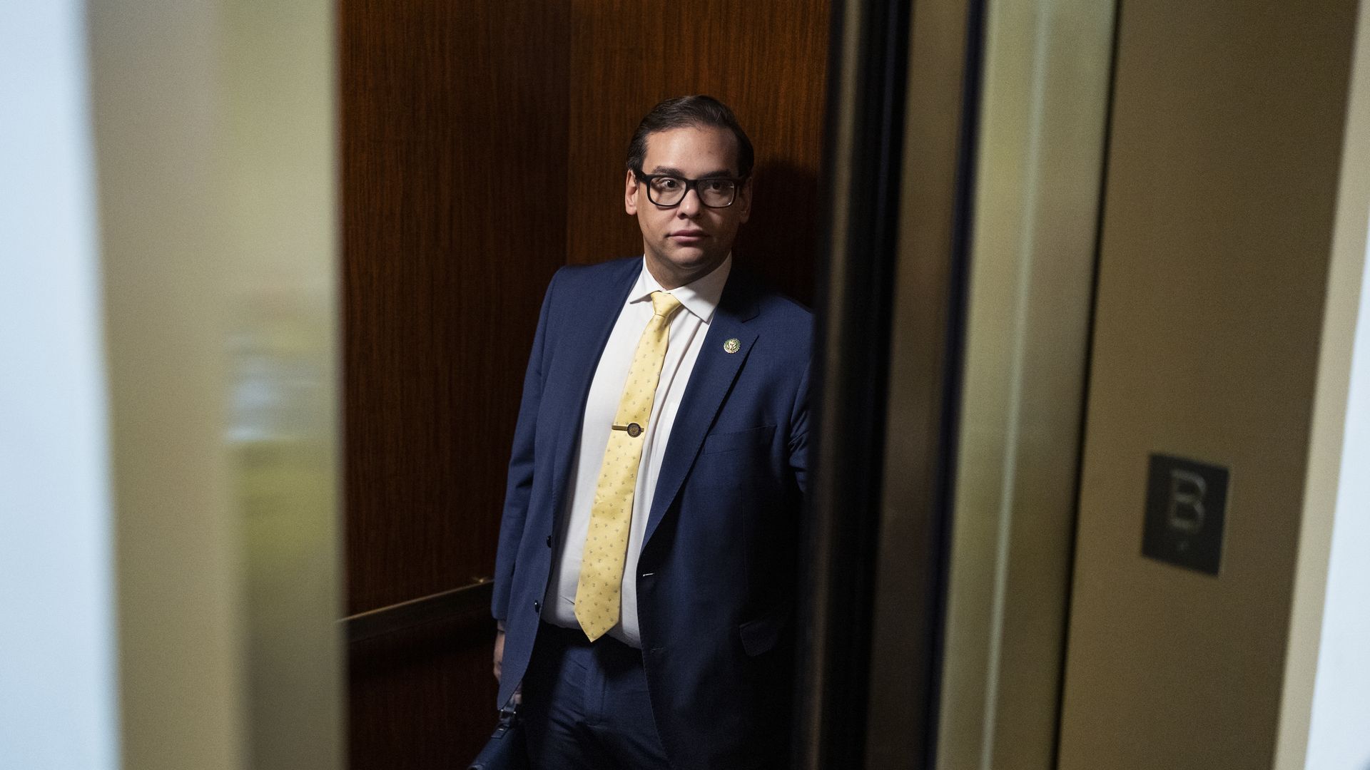 Rep. George Santos, wearing a blue suit jacket, white shirt and yellow tie, stands in an elevator at the Capitol.