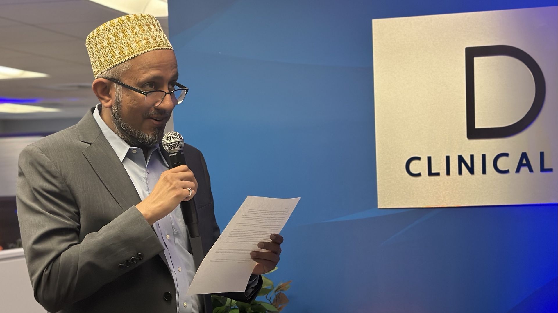 Mohammad Millwala, CEO of DM Clinical Research, reads remarks he printed out on a piece of white paper at the grand opening of the Brookline site.