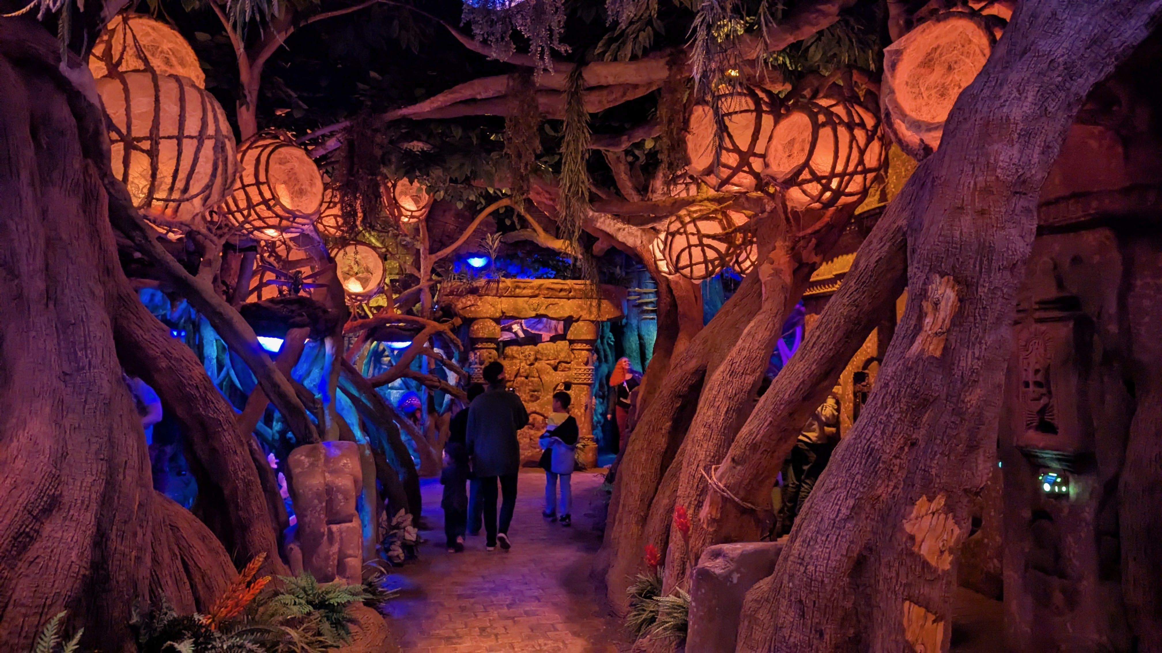 An immersive attraction includes glowing bulbs wrapped in vines and decorations simulating ancient ruins.