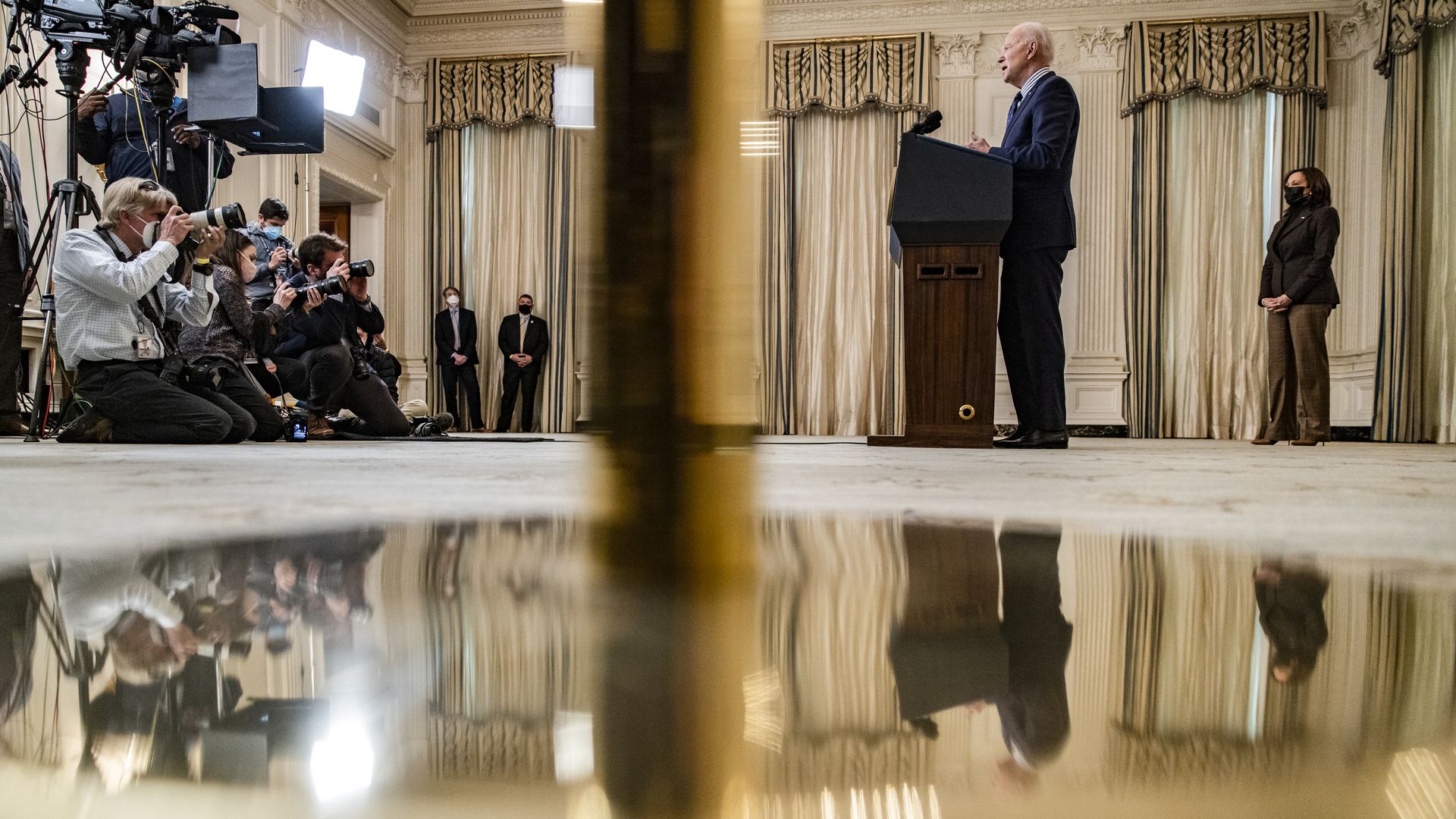 President Biden is seen reflected in a flag stand as he speaks about the Senate's passage of his COVID relief package.
