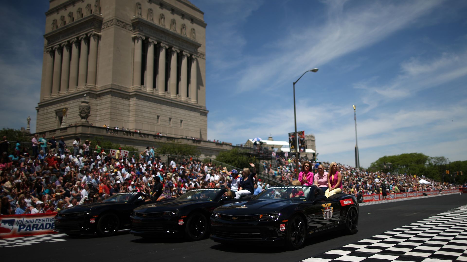 A crowd looks on as cars drive past a checkered road