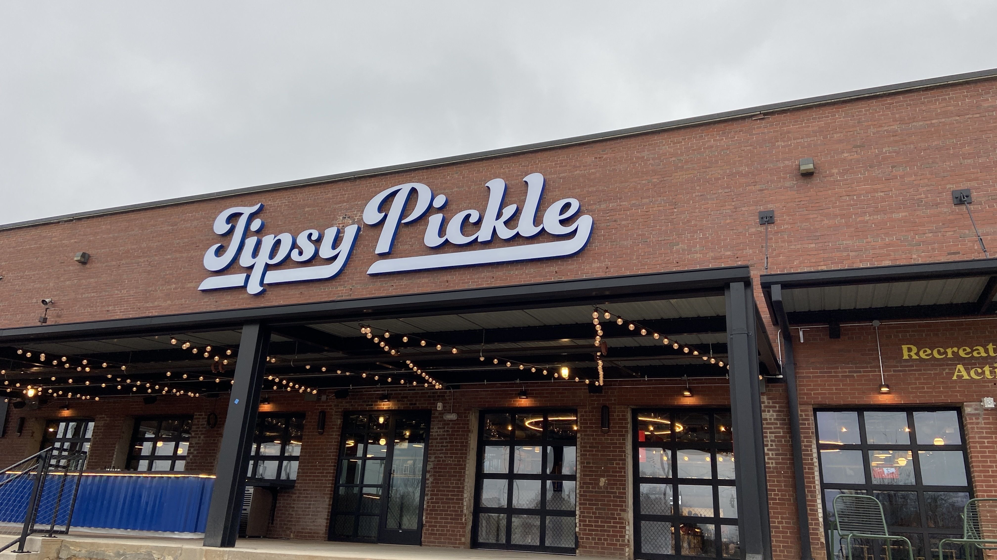 The patio and outdoor bar at Tipsy Pickle at Camp North End. A large sign says "Tipsy Pickle." 