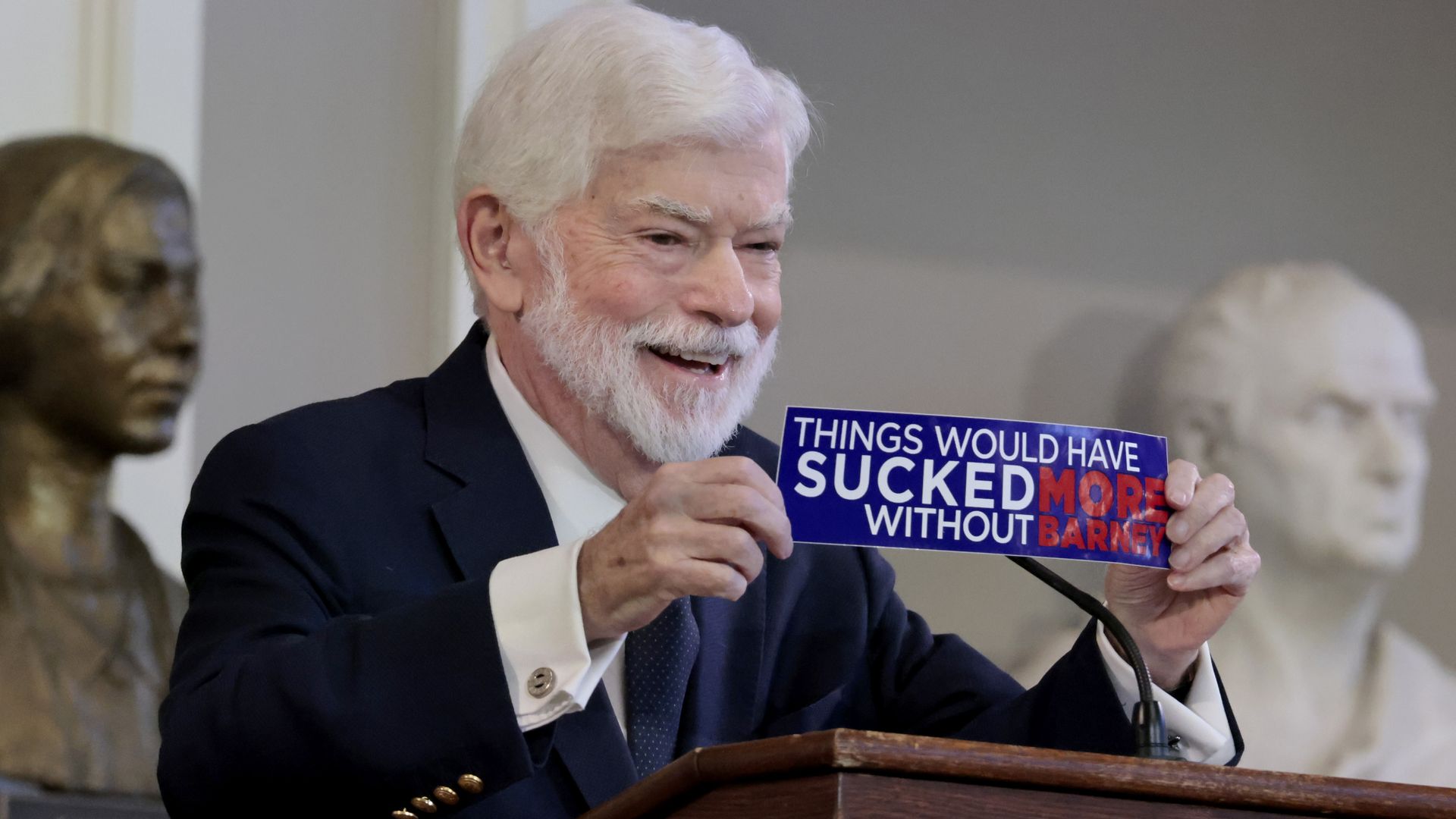 Chris Dodd, former chair of the Senate Banking Committee, holds up a bumper sticker that reads "Things would have SUCKED more without Barney" during a celebration of life for Barney Frank at Faneuil Hall on June 8, 2026. 