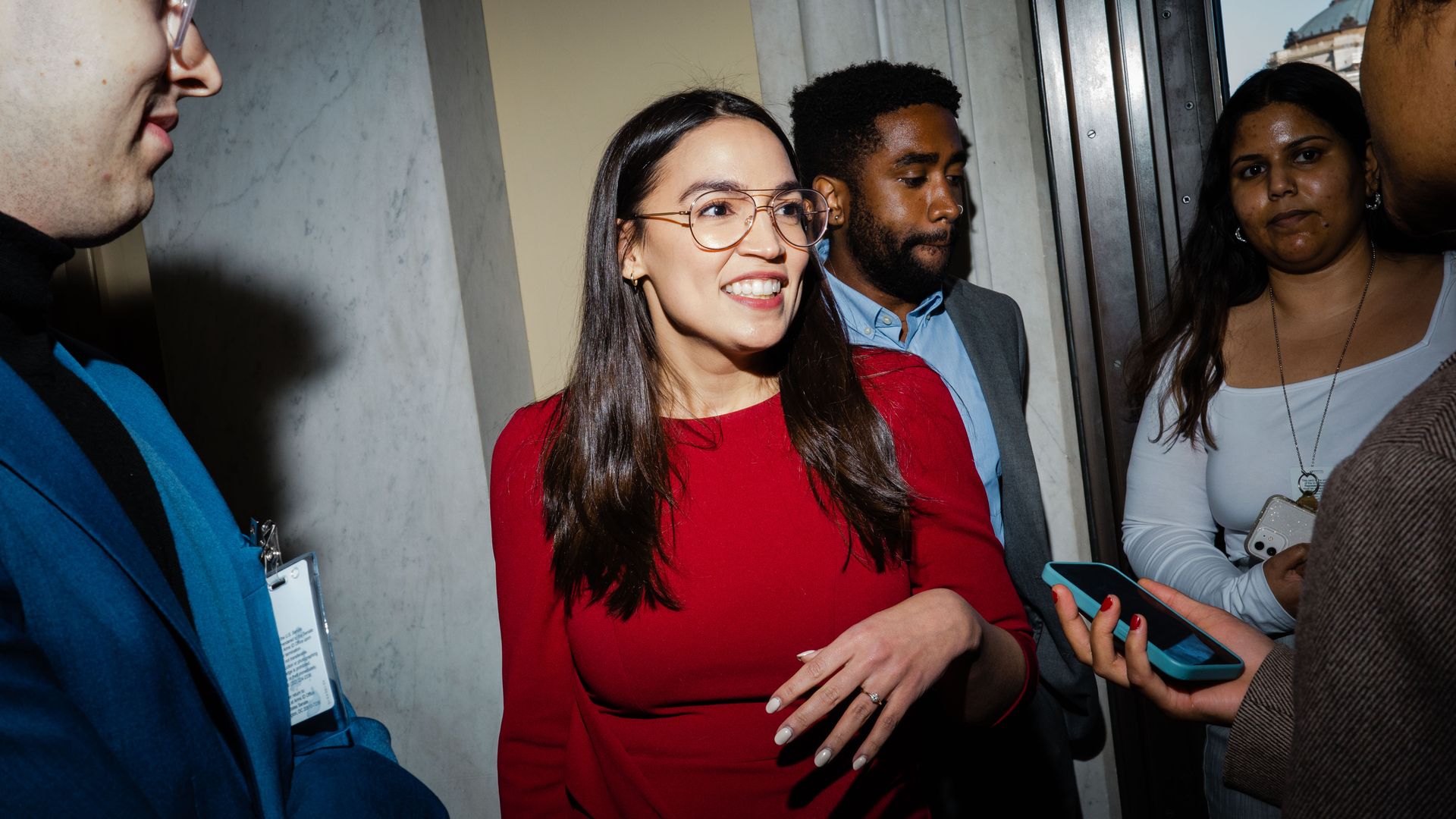 Rep. Alexandria Ocasio Cortez, wearing a red dress and glasses.