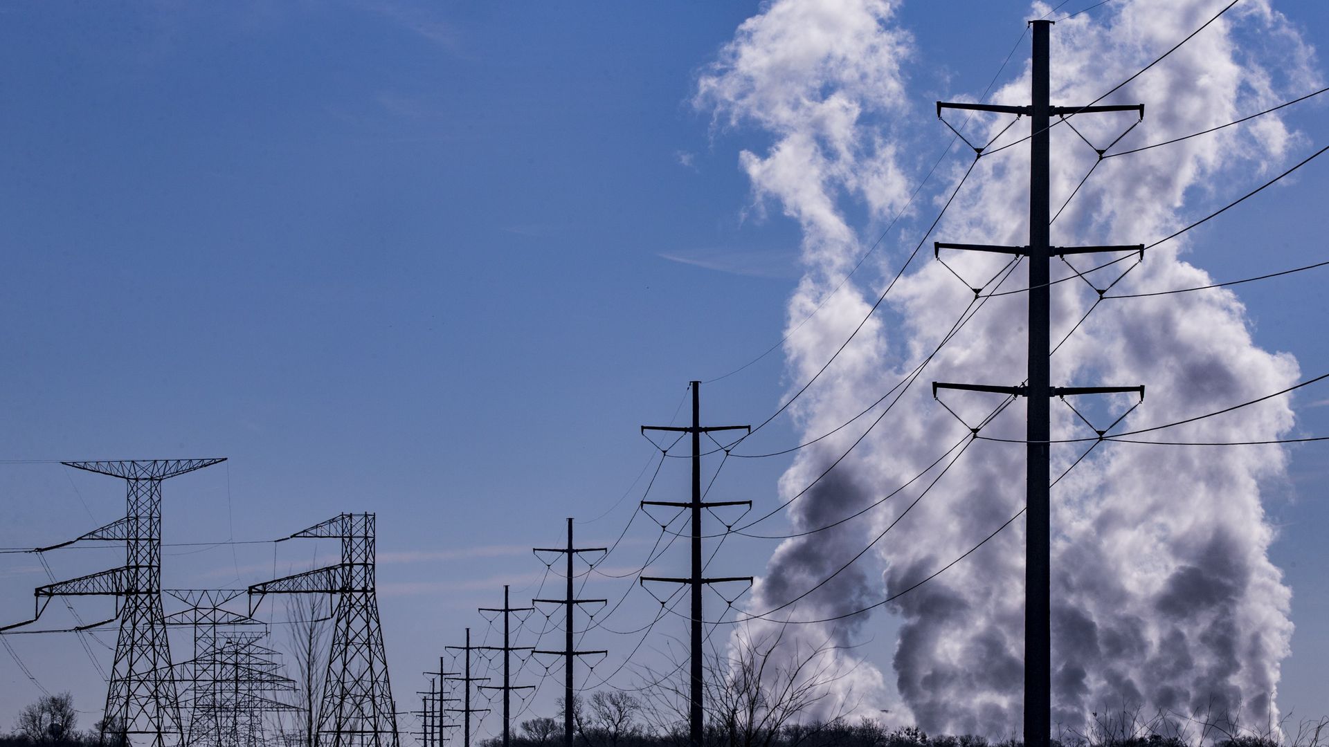 Smoke rises over a power lines, with a clear blue sky in the background.