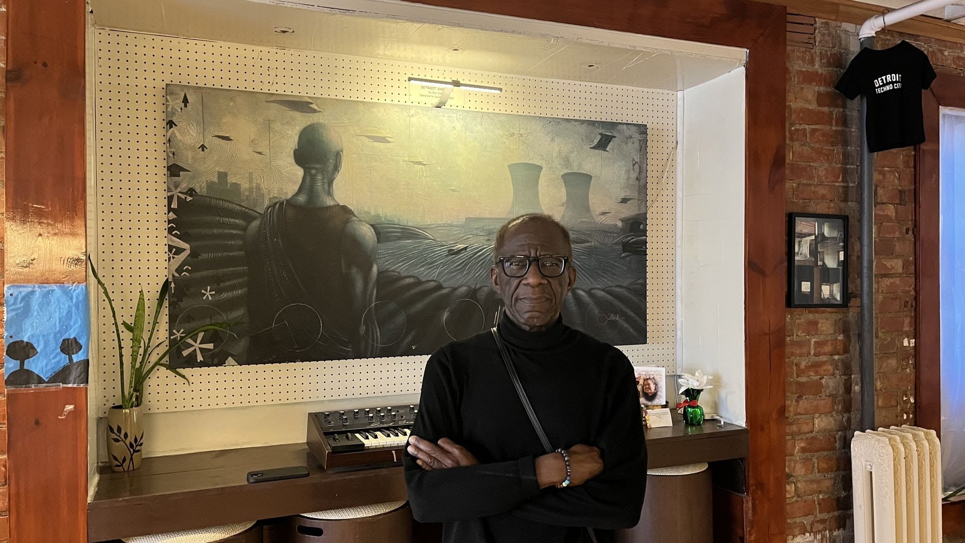 John Collins stands with arms crossed in front of techno memorabilia including futuristic wall art