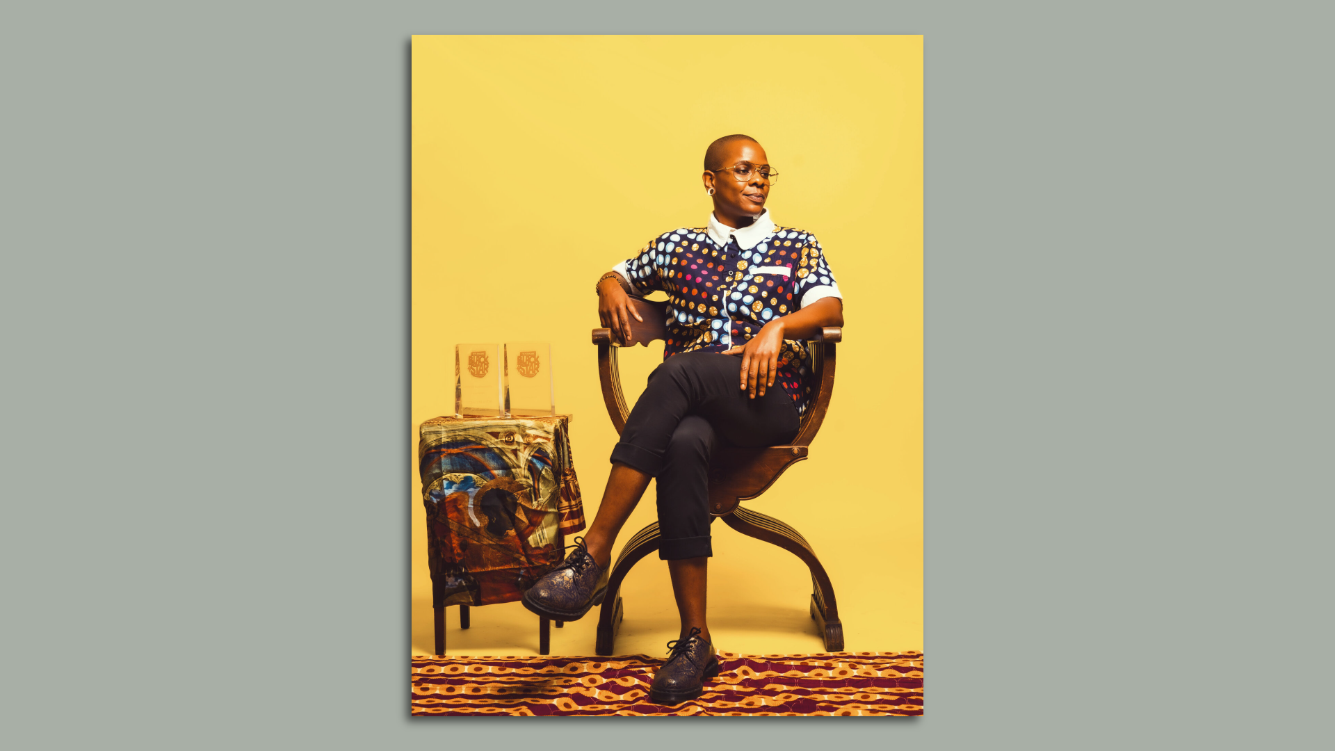 Zuri Obi poses for a photo while sitting in a chair against a yellow background.