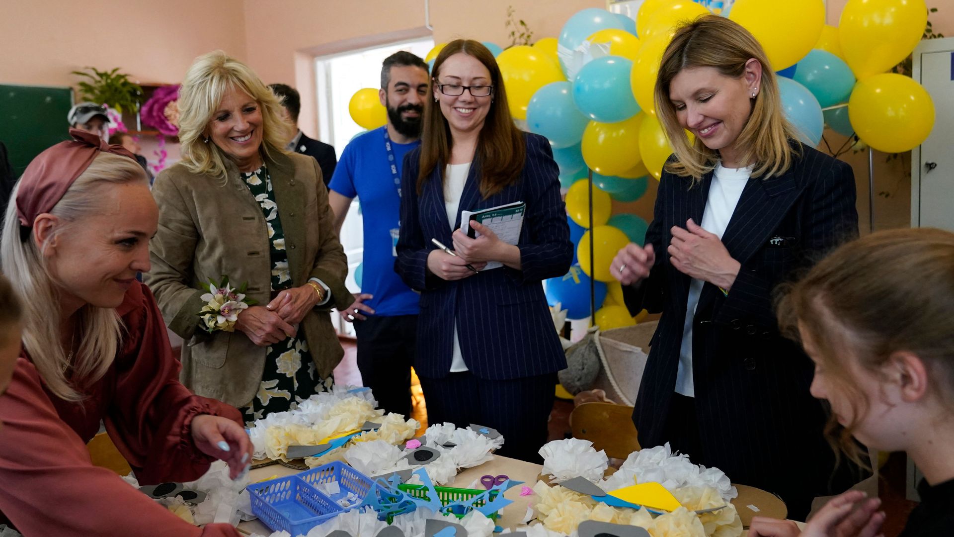 The first ladies of the U.S. and Ukraine are seen watching a girl assemble flowers.