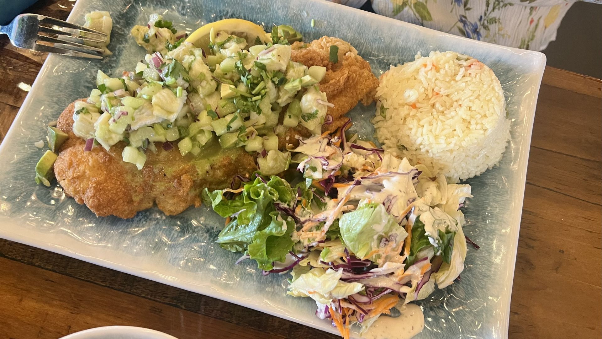 A blue rectangular plate holding a fried fish fillet topped with ceviche with cucumber, and a side salad and pat of rice on the side from Aguazul in San Antonio.