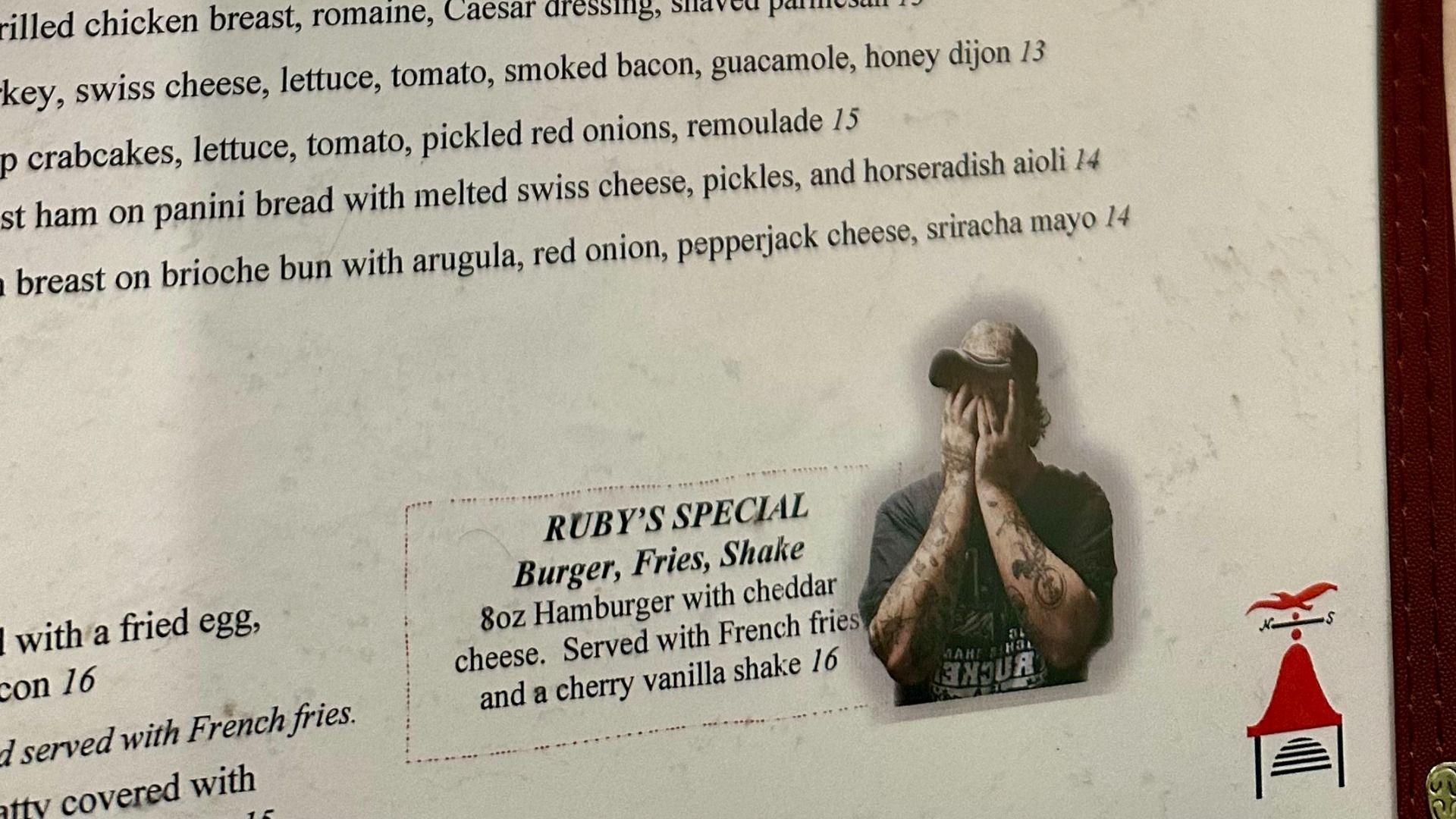 Menu page showing burger items and a dashed box reading "RUBY'S SPECIAL"; a tattooed man in a cap covers his face with his hands in the lower right.