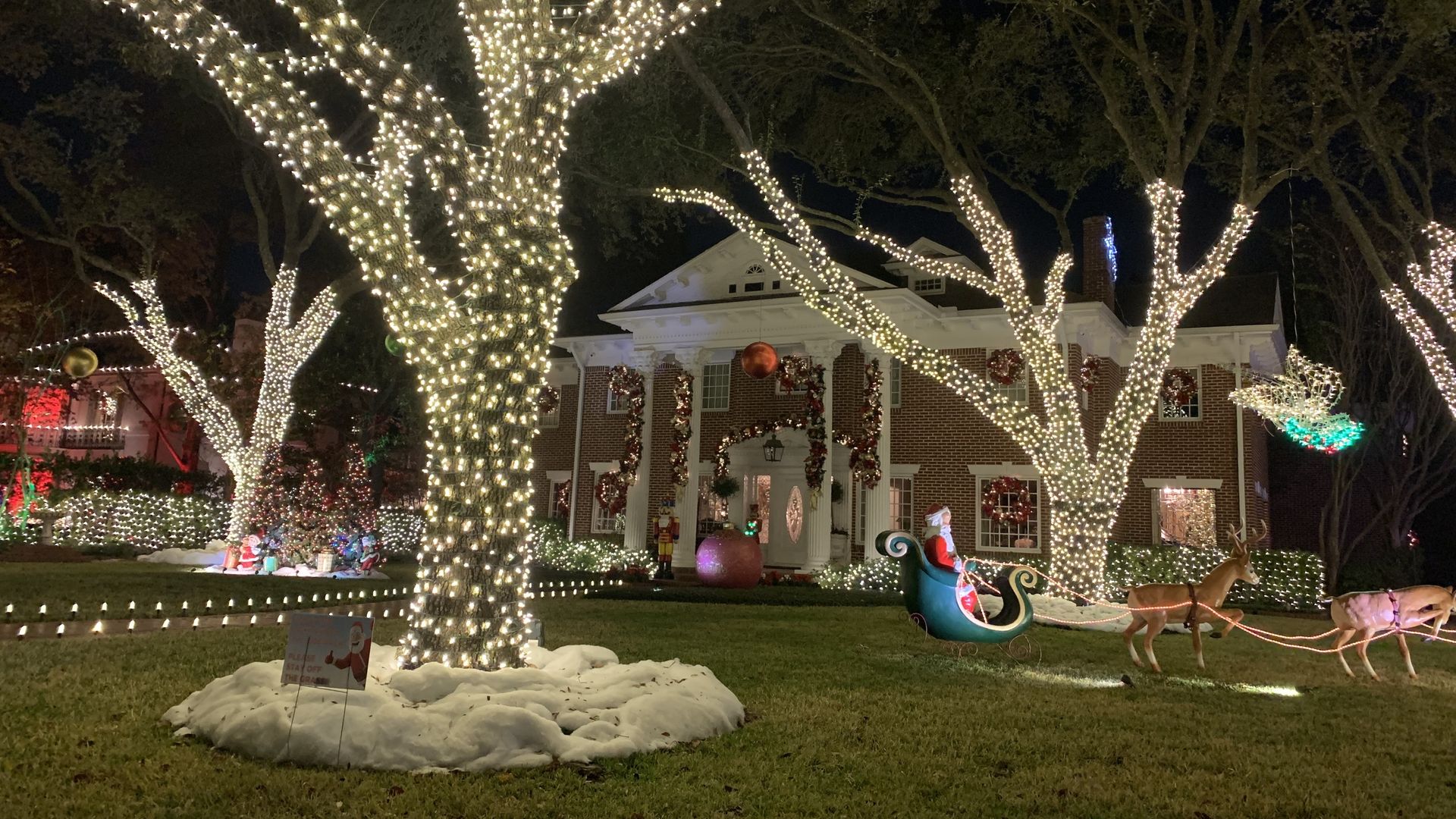 Several trees wrapped in white holiday lights in the front yard of a massive home in Houston's River Oaks neighborhood 