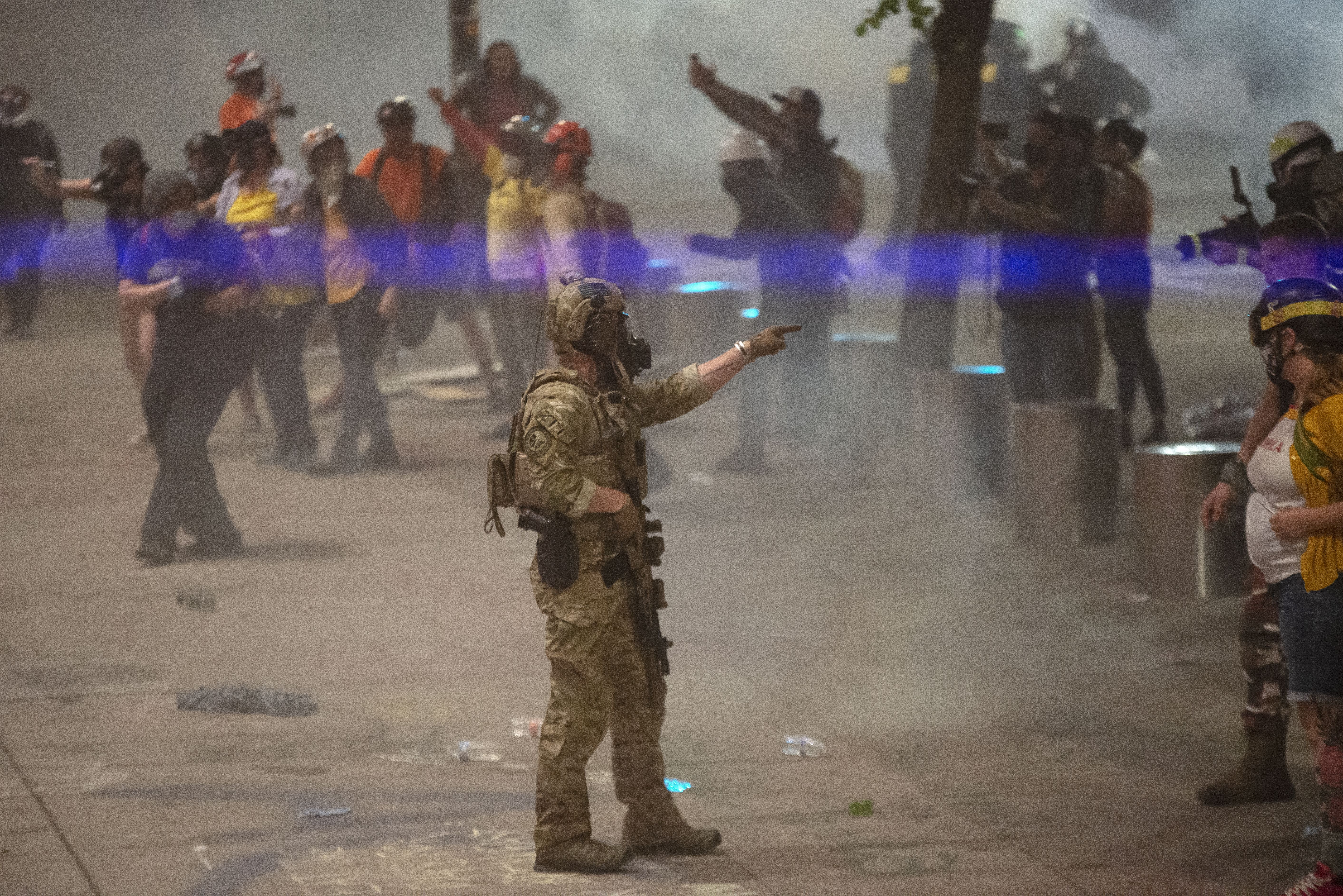 A federal officer points at a protester with tear gas in the background