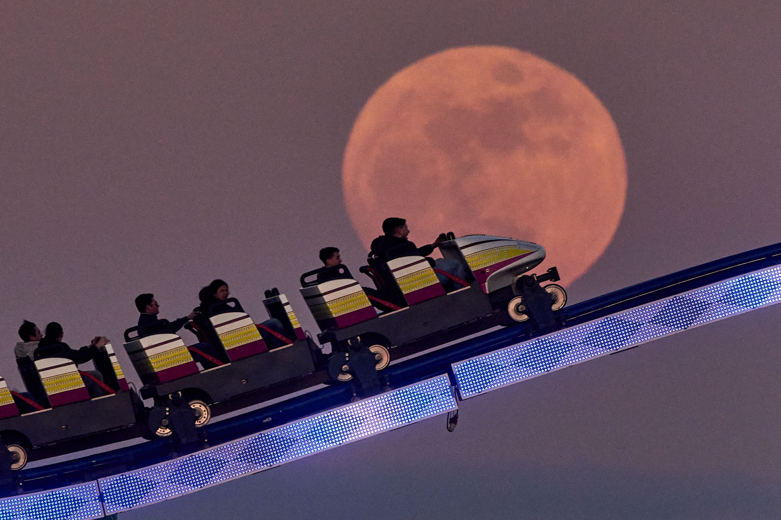 People ride a roller coaster past the full moon on the funfair in Frankfurt