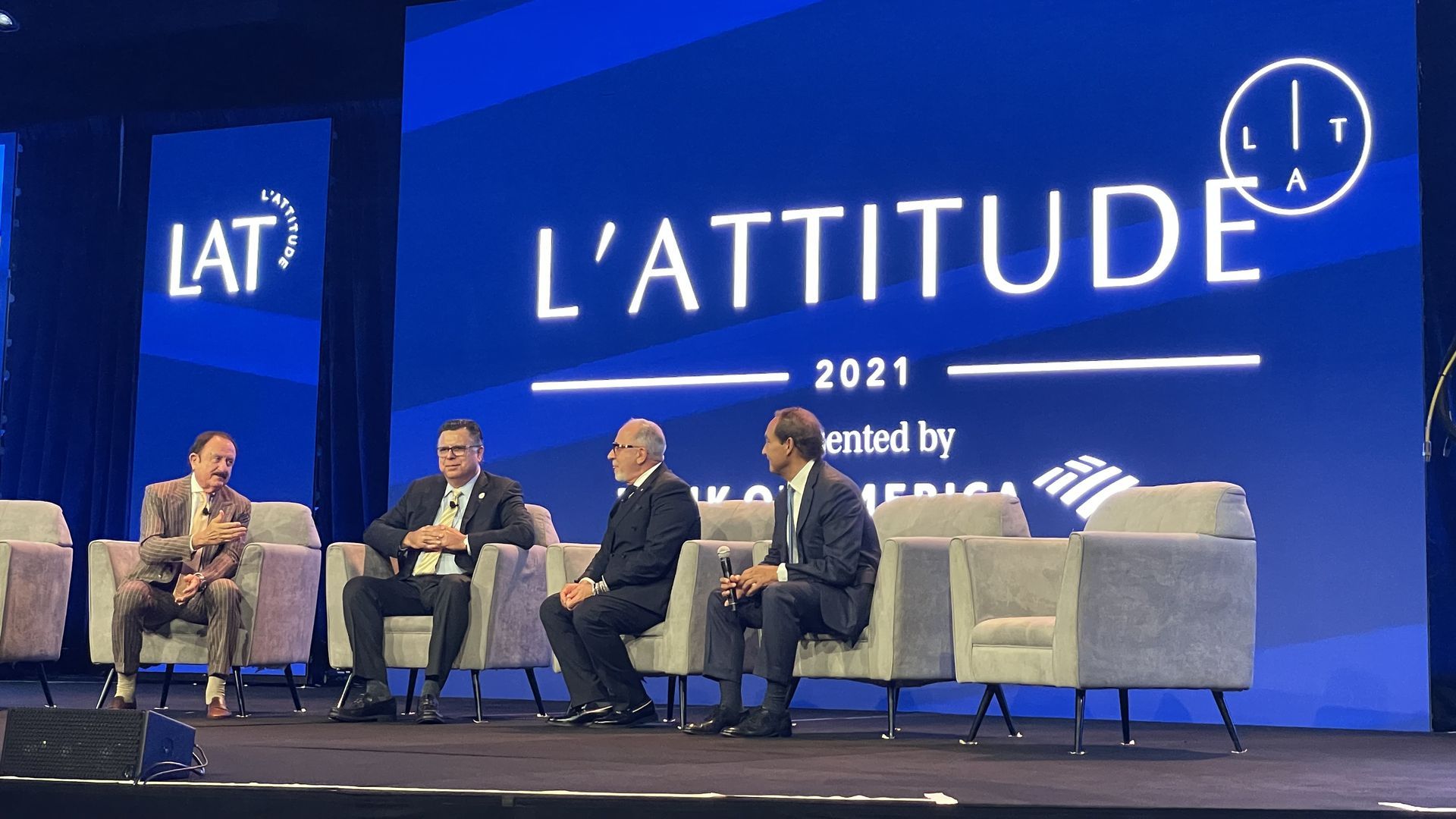Four men in suits on the stage at the L'attitude conference. 