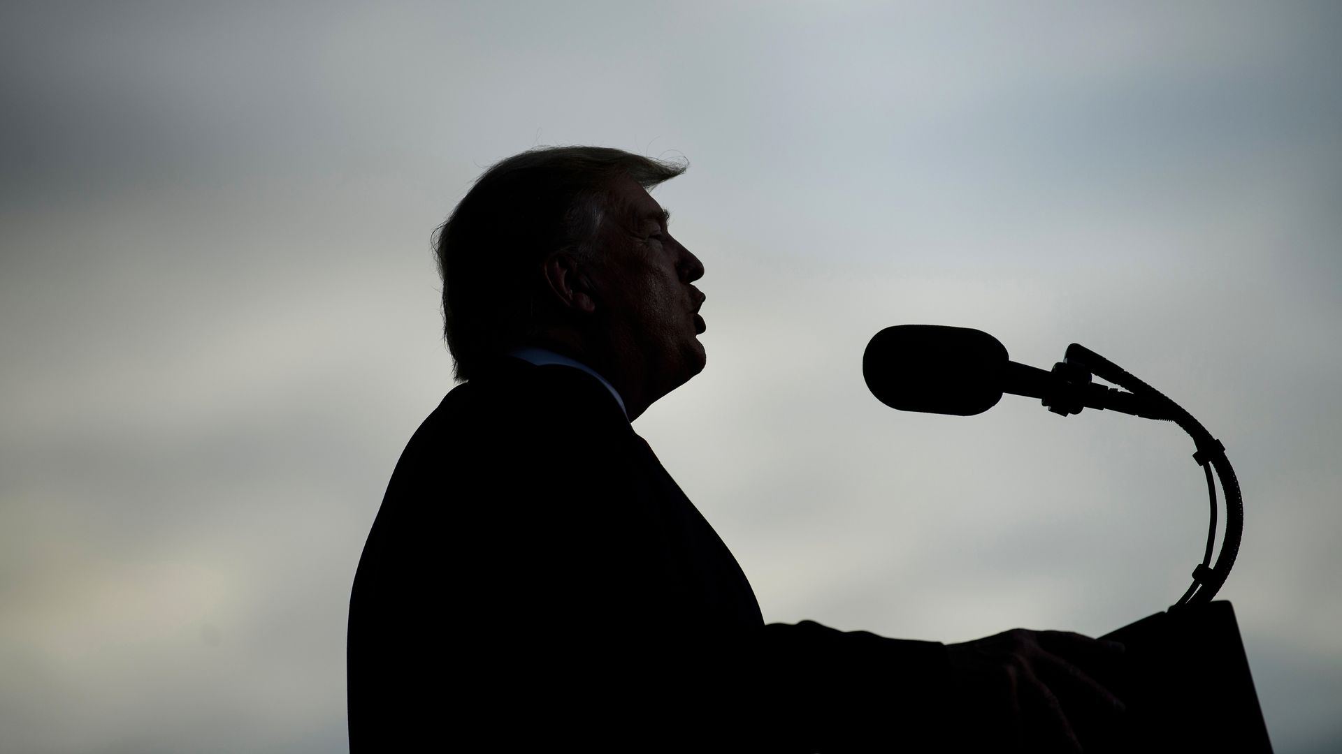 In this image, Trump's silhouette is visible as he speaks into a microphone 