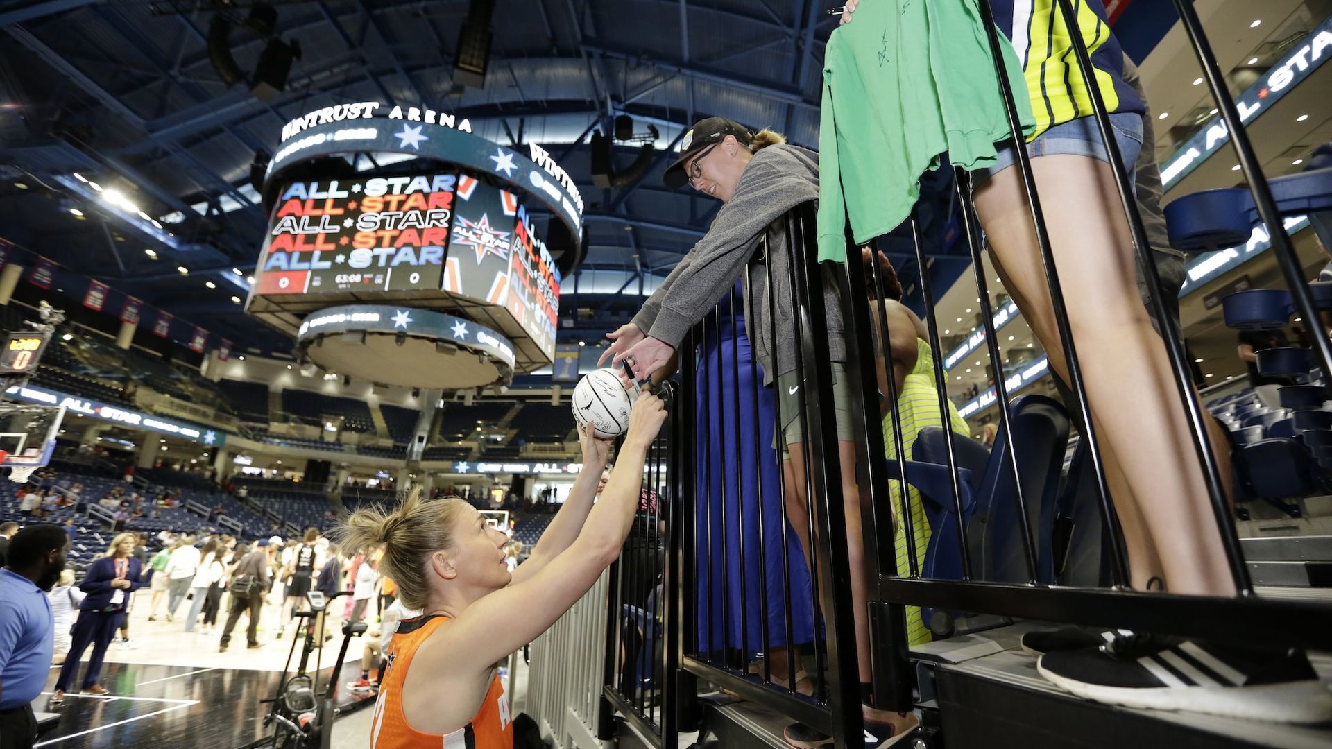 Courtney Vandersloot in orange jersey stretches her arms up to fans in the stands to autograph a basketball.
