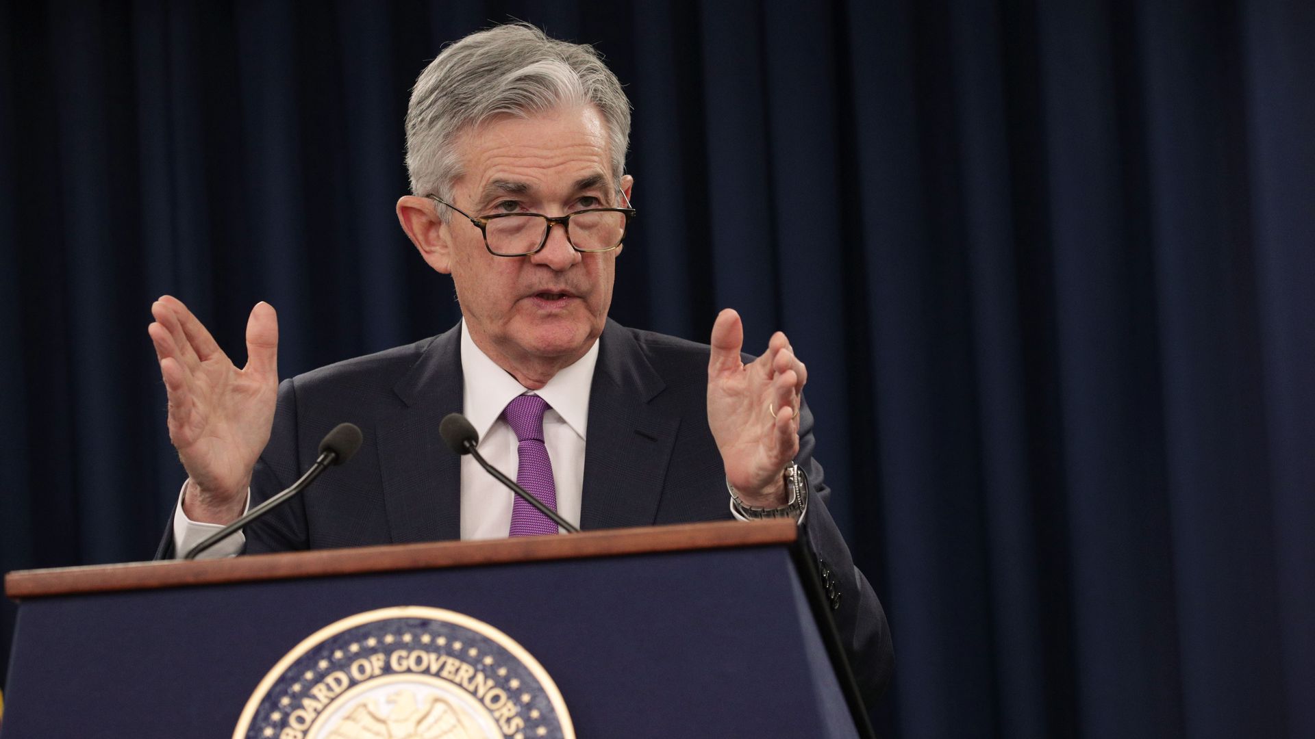 In this image, Federal Reserve Board Chairman Jerome Powell speaks into two microphones from behind a podium.
