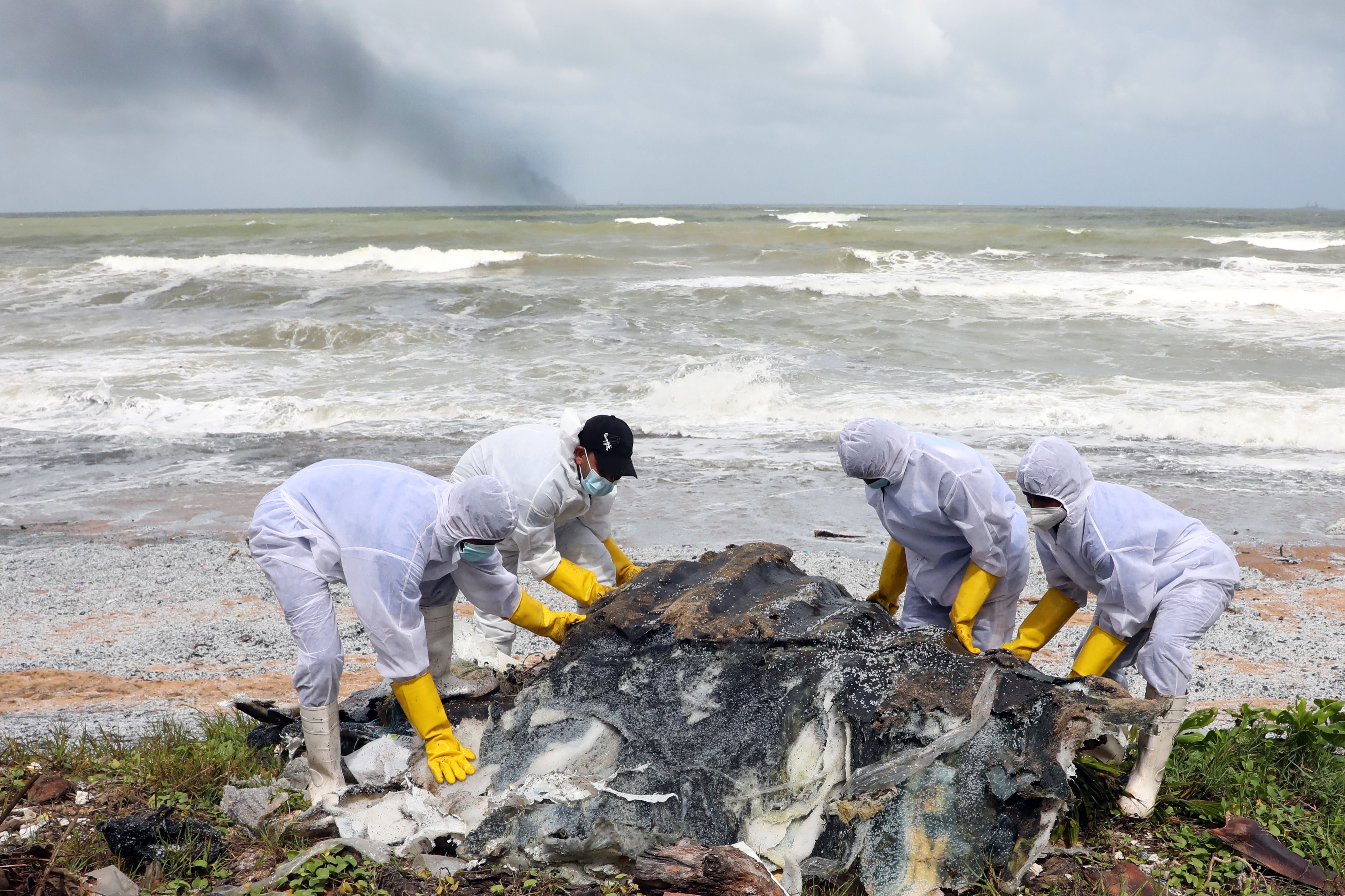 Sri Lanka Navy personnel in protective clothing pull ashore the metal remnants of a container washed ashore from the burning cargo vessel 