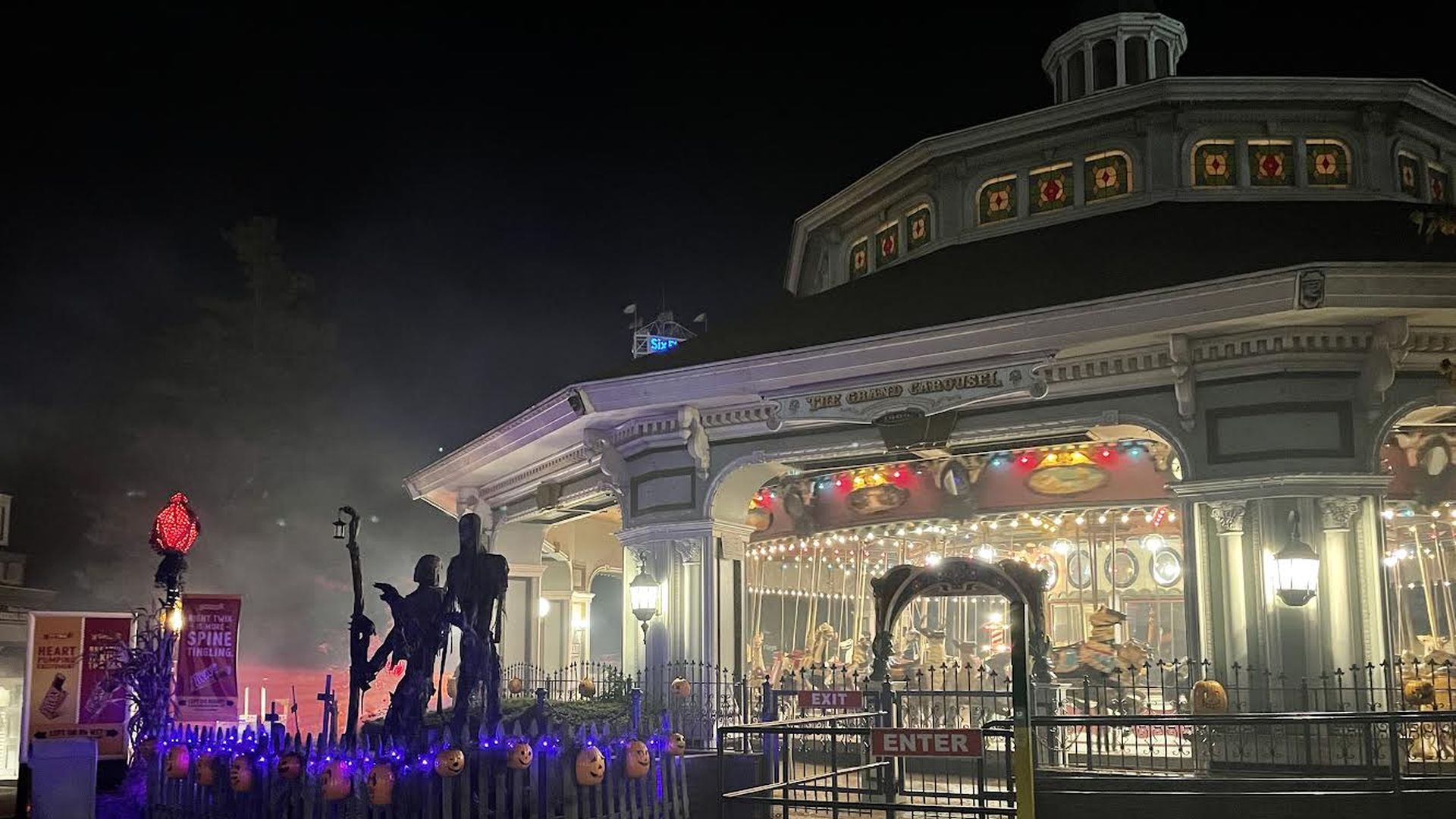 Two hooded skeletons stand in front an empty merry go round at night in Six Flags.