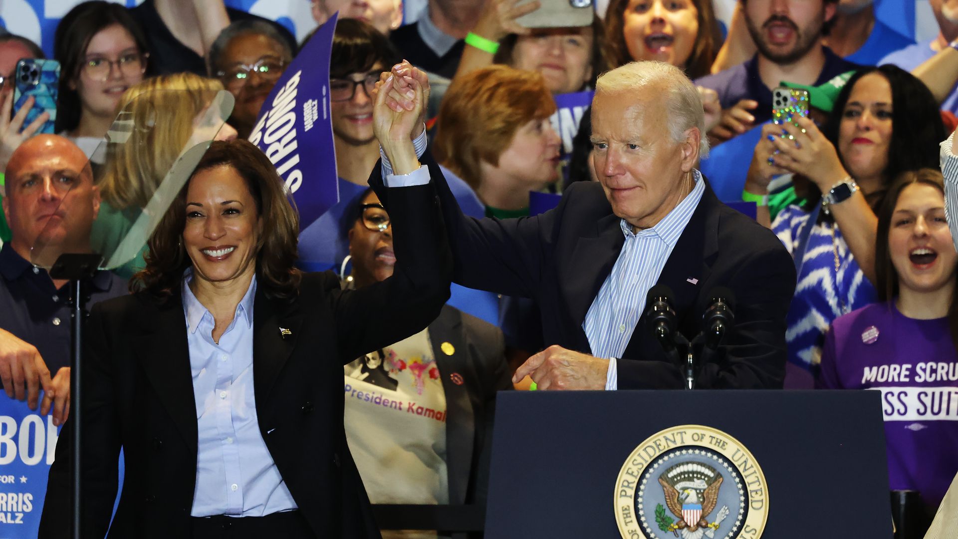 Harris and Biden hold hands in the air while at a campaign event. Fans are seen cheering in the background.