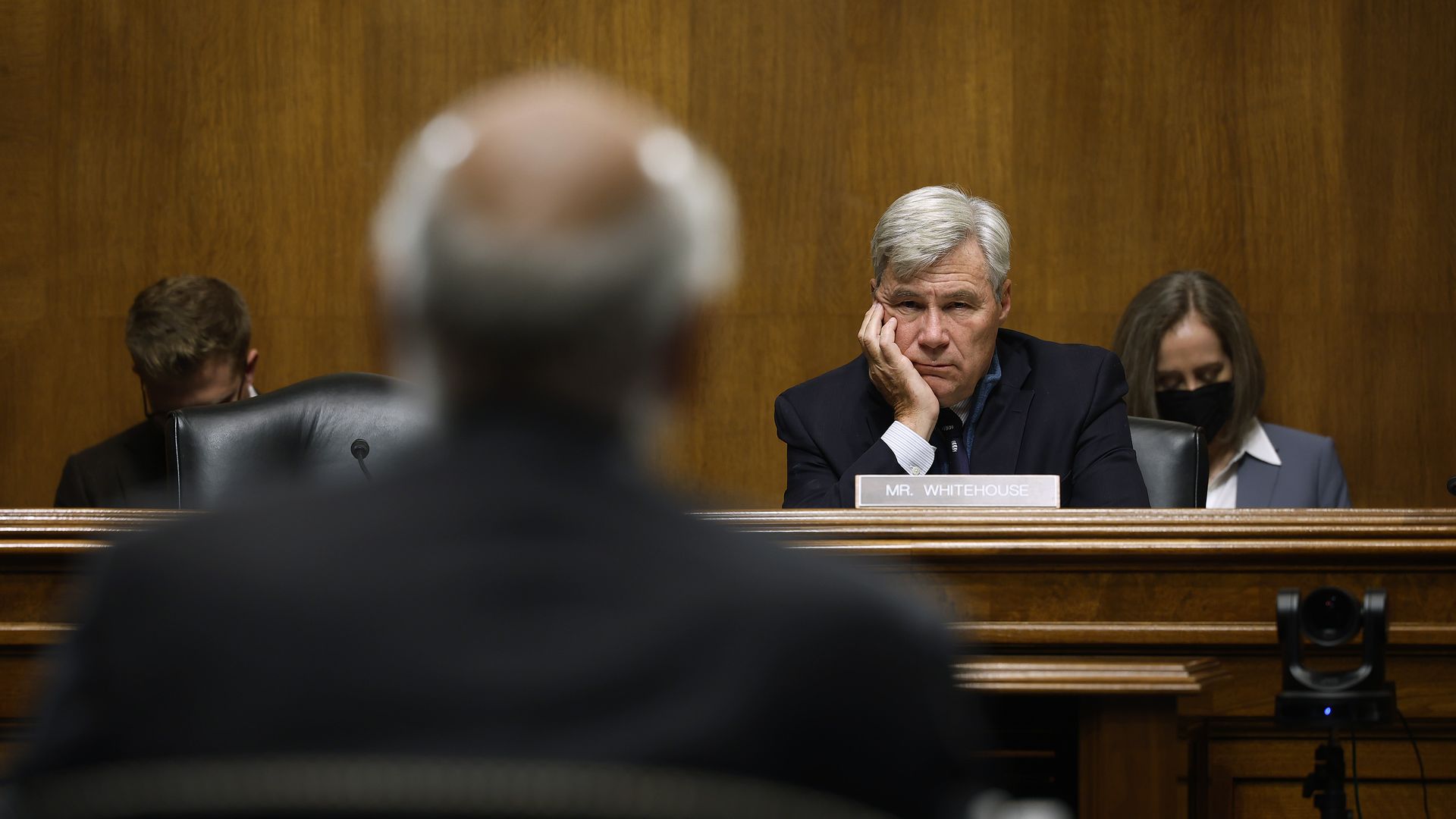 Sen. Sheldon Whitehouse, sitting behind the dais at a committee hearing wearing a dark blue suit.