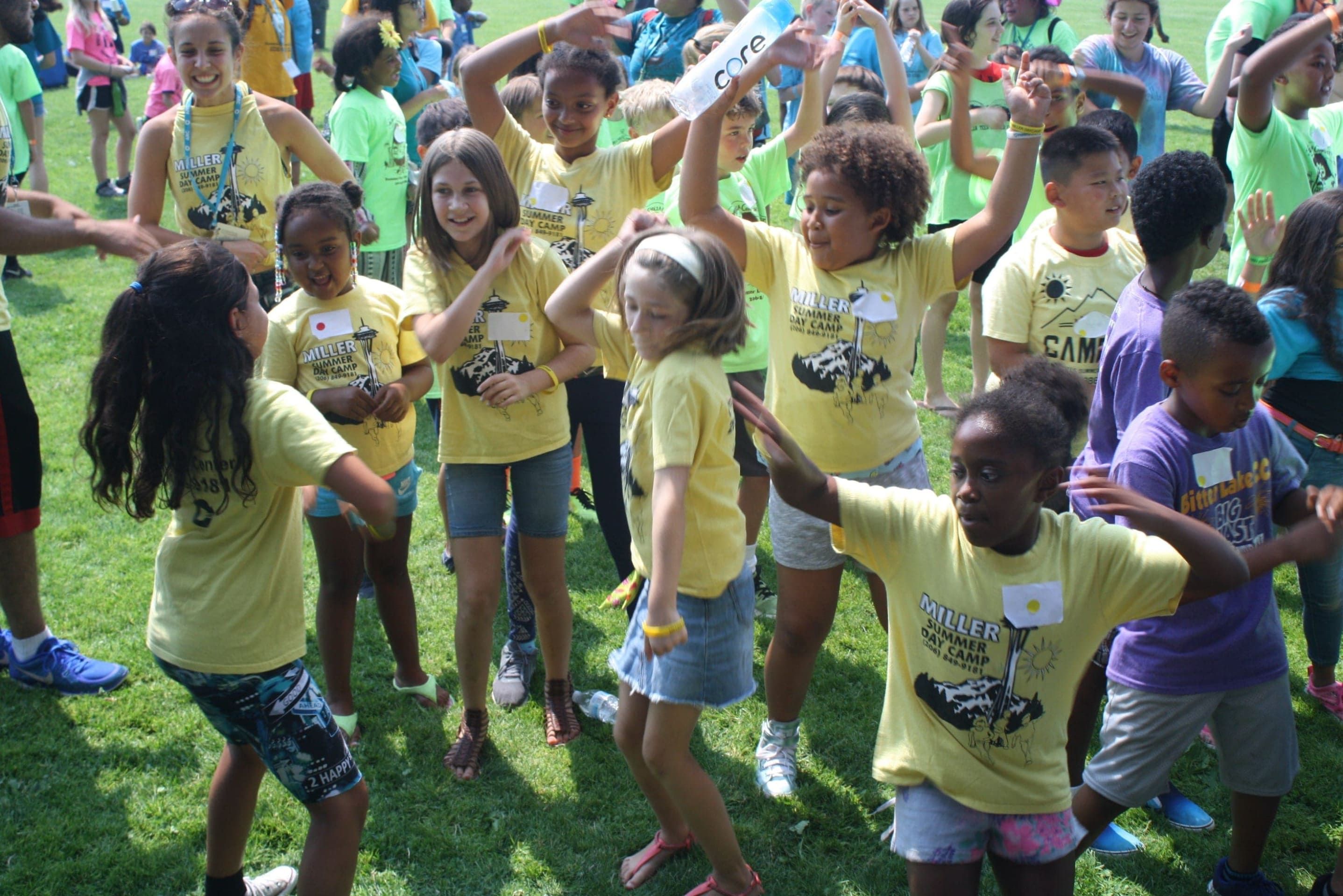 KIds in yellow and purple t-shirts dance and play at a Seattle summer camp. 