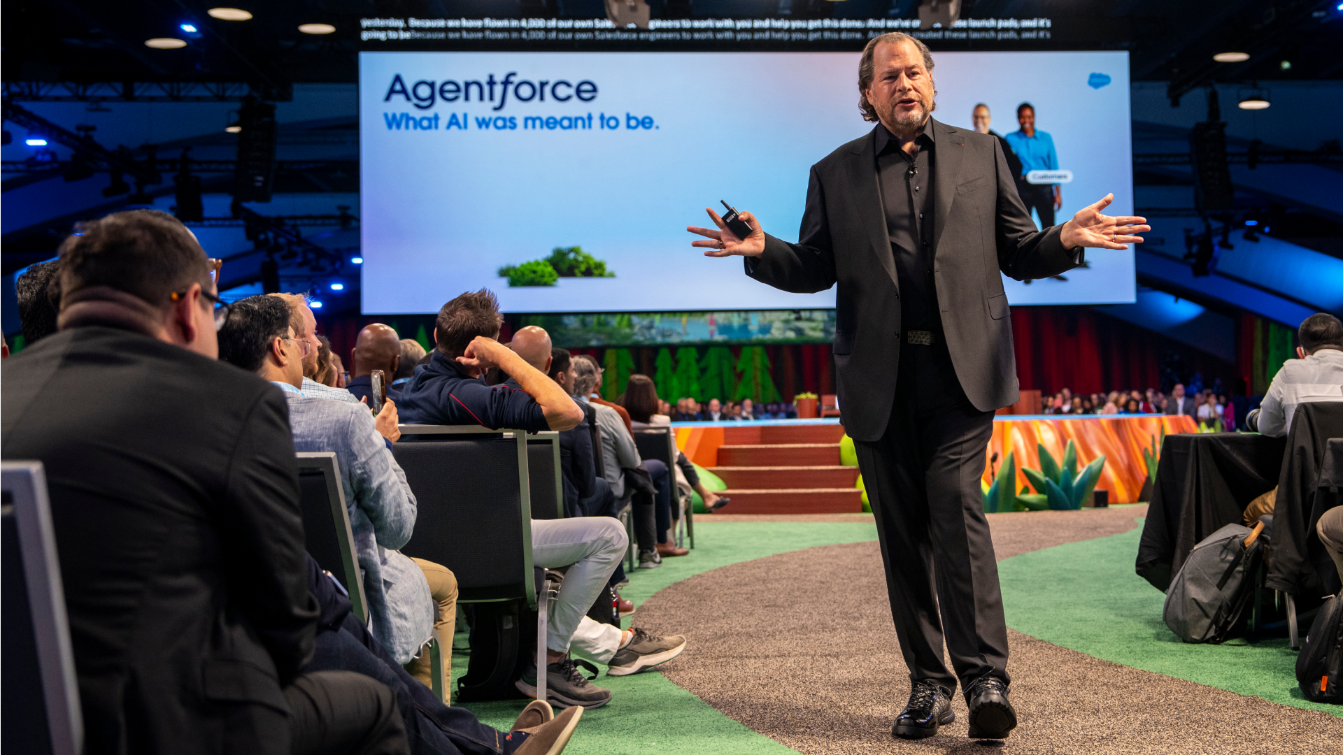 A man in a black suit talking to an audience. There is a presentation behind him.