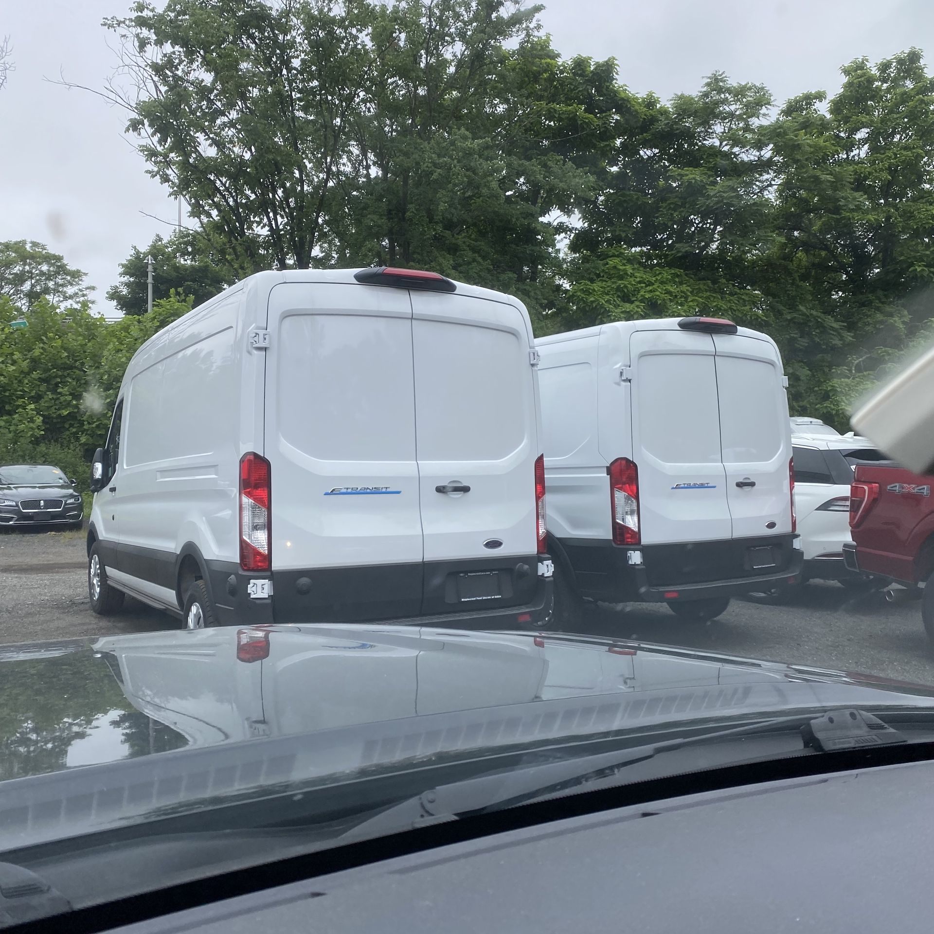 A photo of two Ford E-Transit electric vans, parked in a dealer's lot.